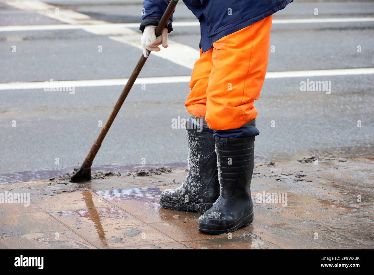 Worker breaks ice and melting snow on the road with a crowbar. Snow removal in city, street cleaning in early spring Stock Photo