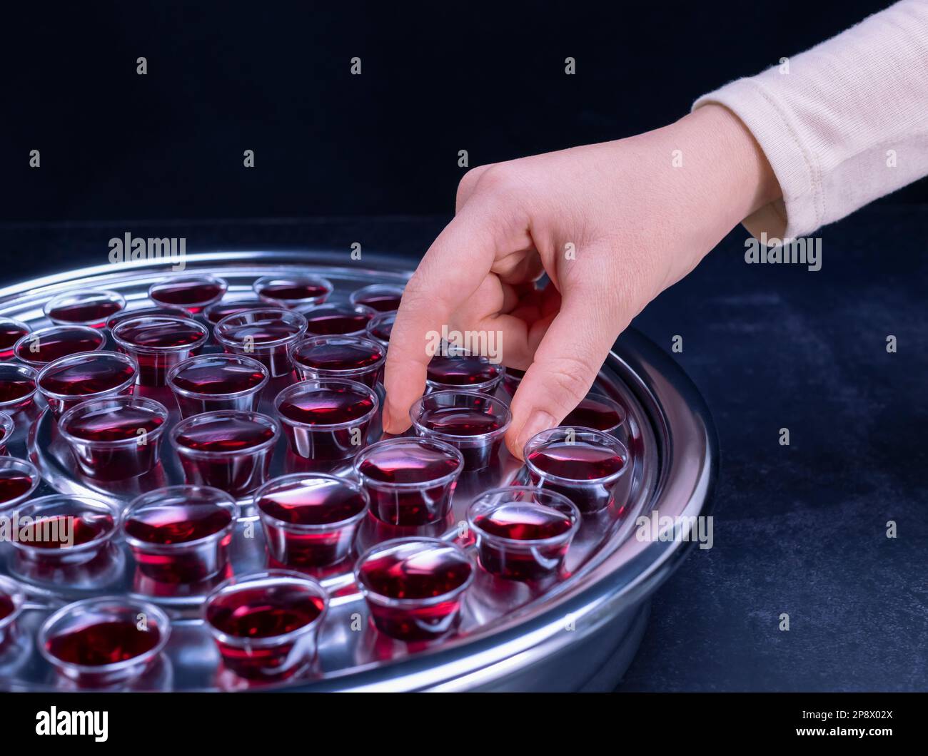 Closeup of young woman taking communion the wine symbol of Jesus Christ blood in small cups on black background. Easter Passover and Lord Supper conce Stock Photo