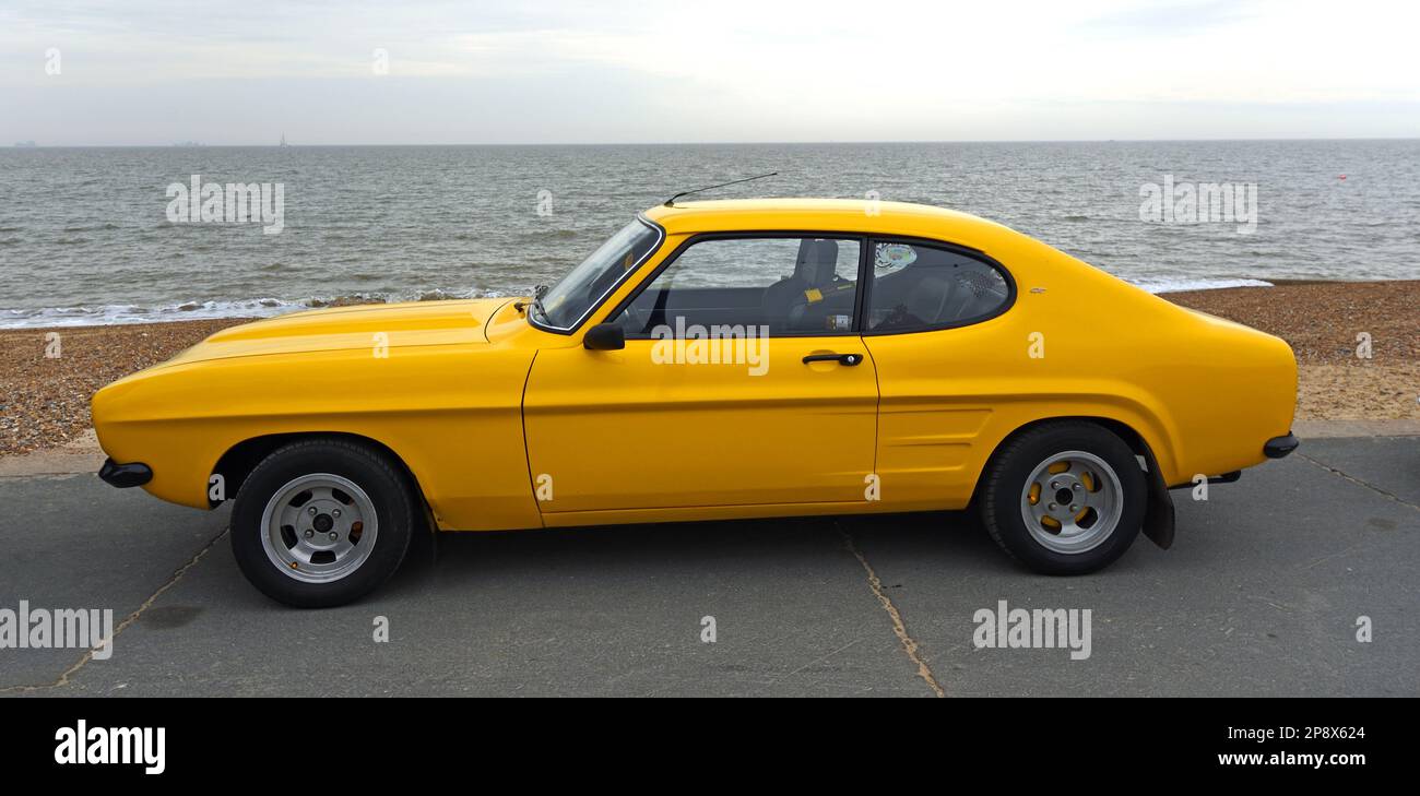 FELIXSTOWE, SUFFOLK, ENGLAND - MAY 01, 2022: Classic Yellow Ford Capri GT Parked on seafront promenade ocean in background. Stock Photo