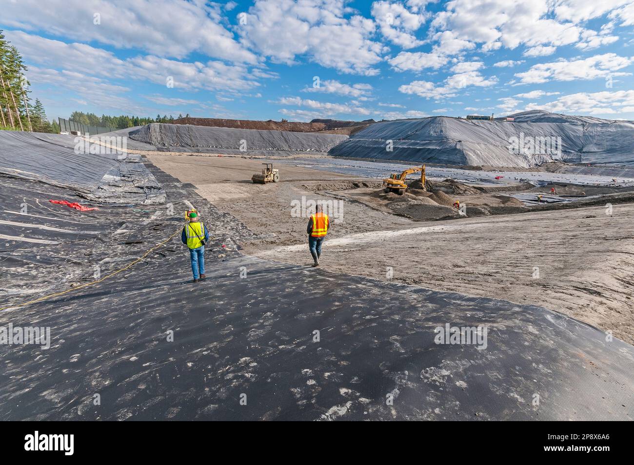 Workers and equipment in vast areas of excavation and plastic geomembrane coverings at an active landfill. Stock Photo