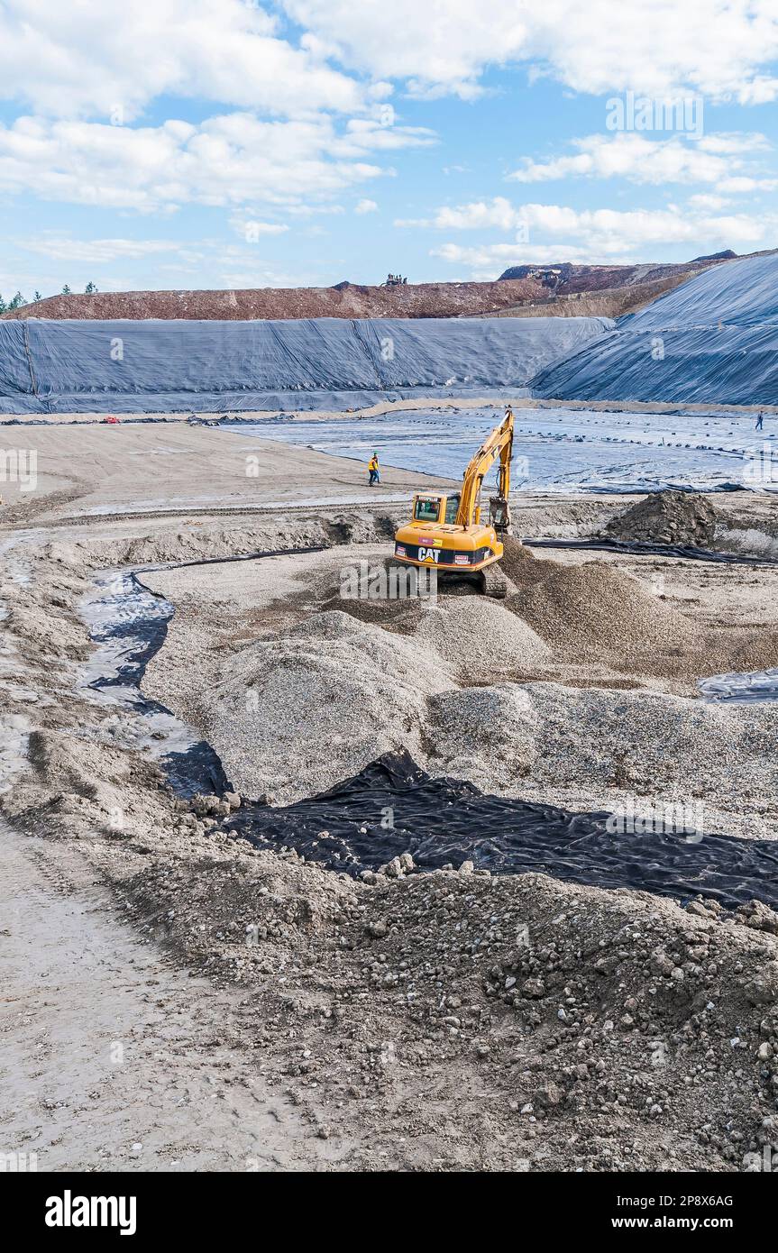 Workers and equipment in vast areas of excavation and plastic geomembrane coverings at an active landfill. Stock Photo