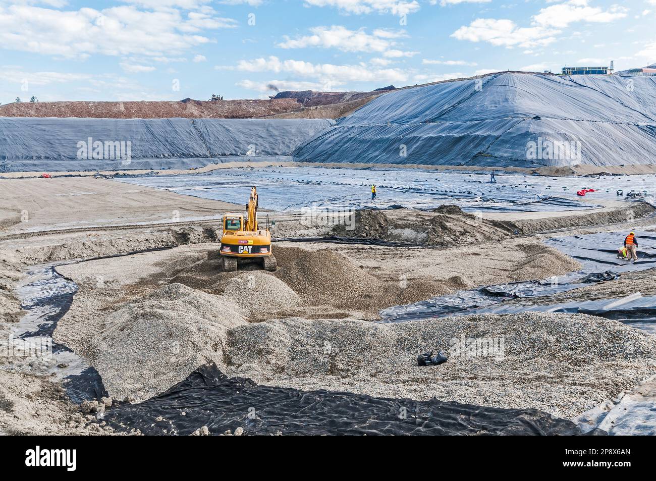 Workers and equipment in vast areas of excavation and plastic geomembrane coverings at an active landfill. Stock Photo