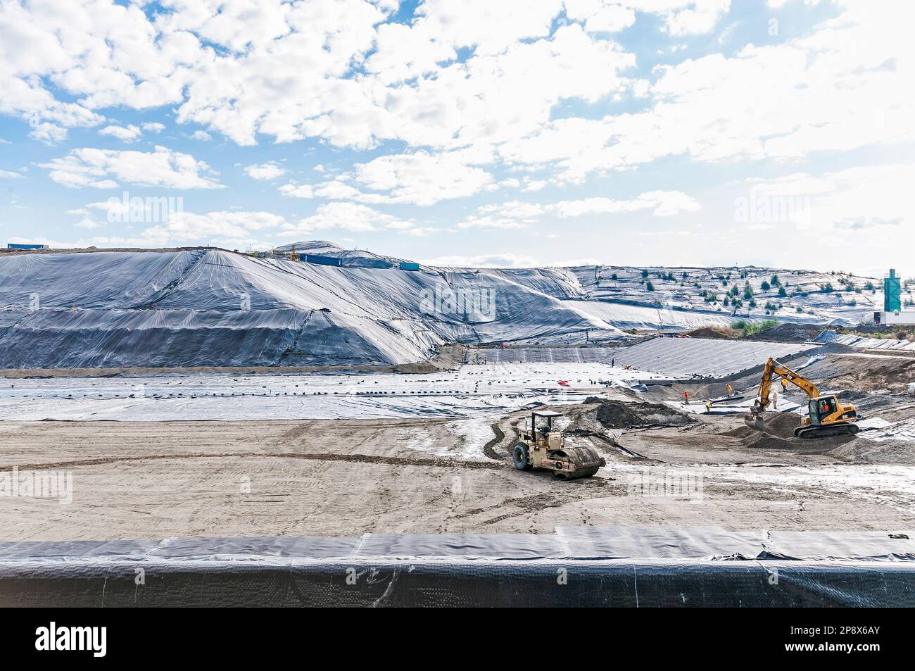 Workers and equipment in vast areas of excavation and plastic geomembrane coverings at an active landfill. Stock Photo