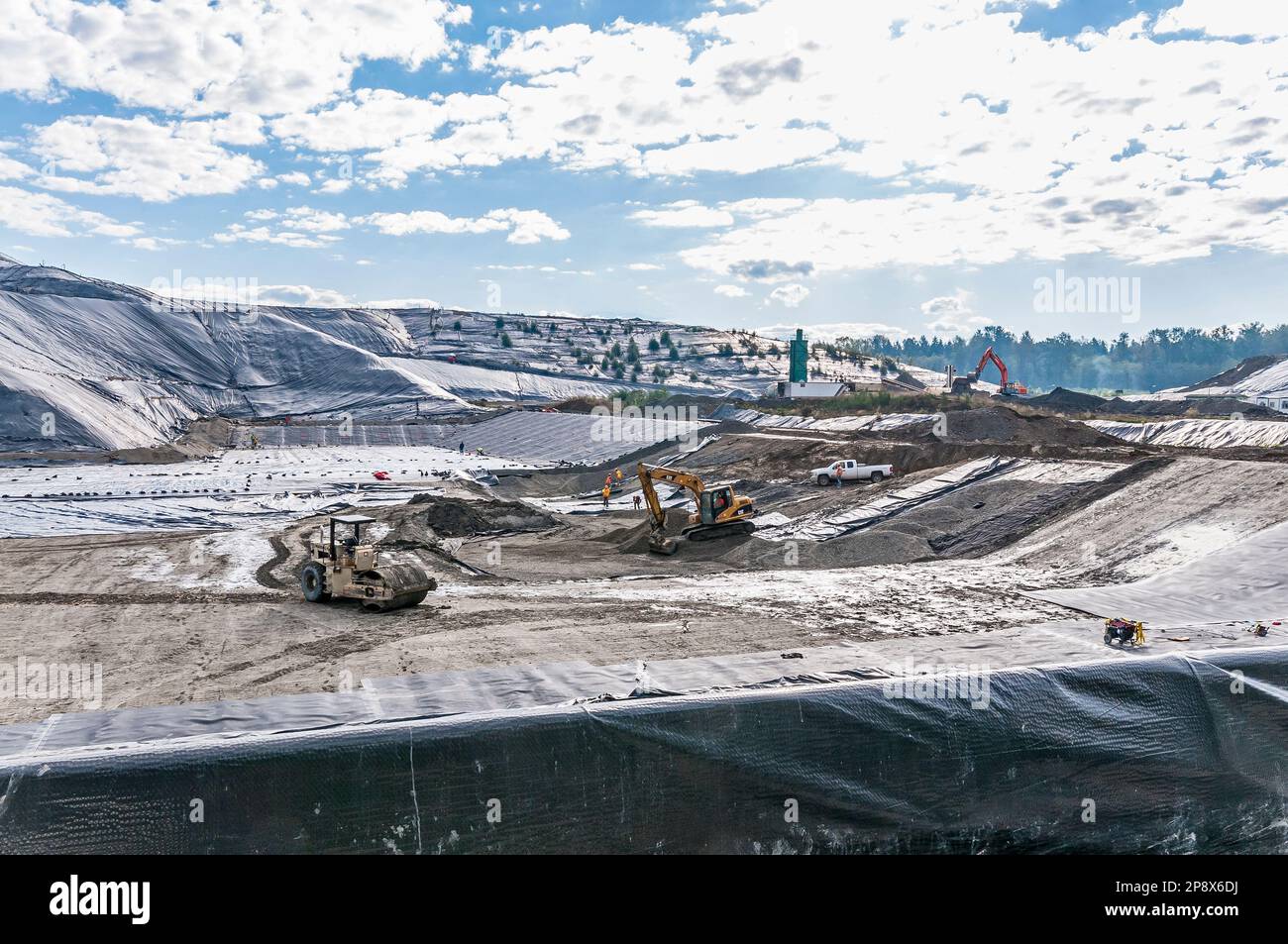 Workers and equipment in vast areas of excavation and plastic geomembrane coverings at an active landfill. Stock Photo