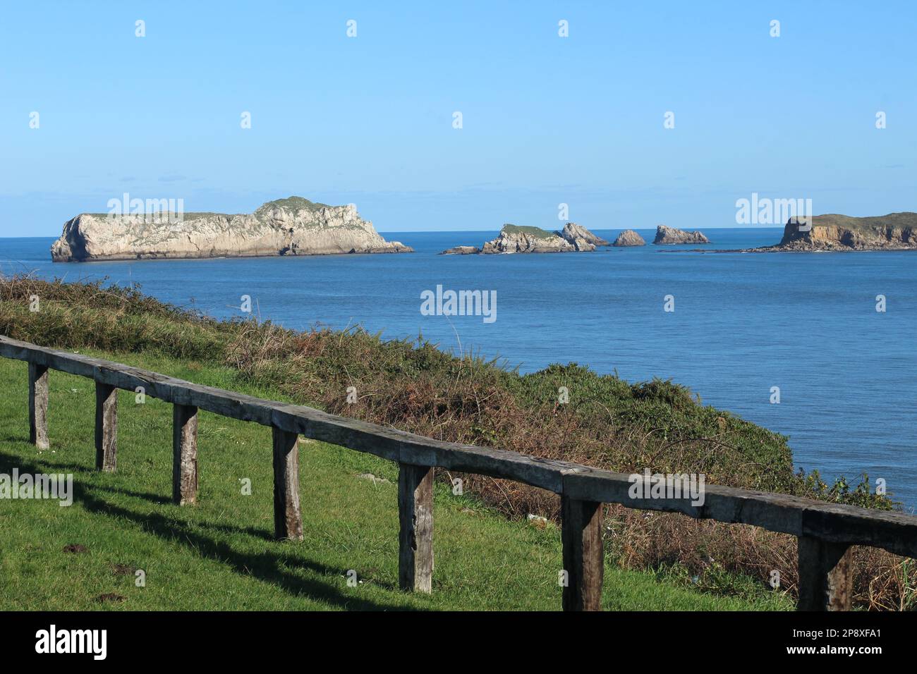 Isla de los Conejos en la villa de Suances, por donde entran las aguas del mar cantábrico a su playa de la Concha, con valla de madera y prado verde. Stock Photo