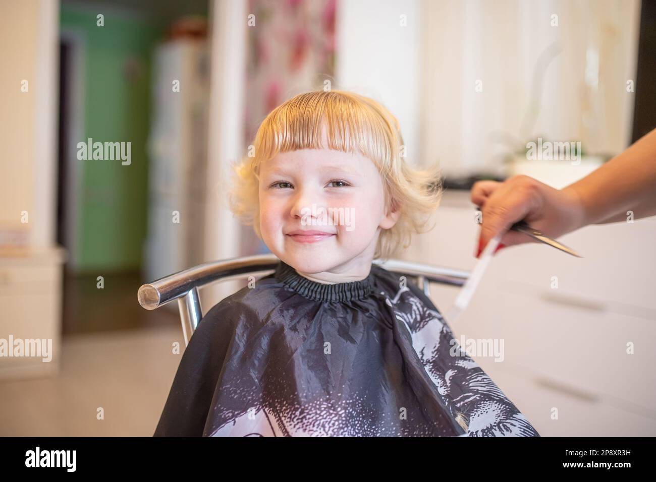 The little curly girl smiles happily after cutting the bangs at home in