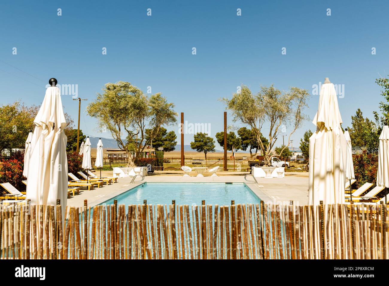 An empty hotel pool during midday sun from behind the bamboo fence Stock Photo