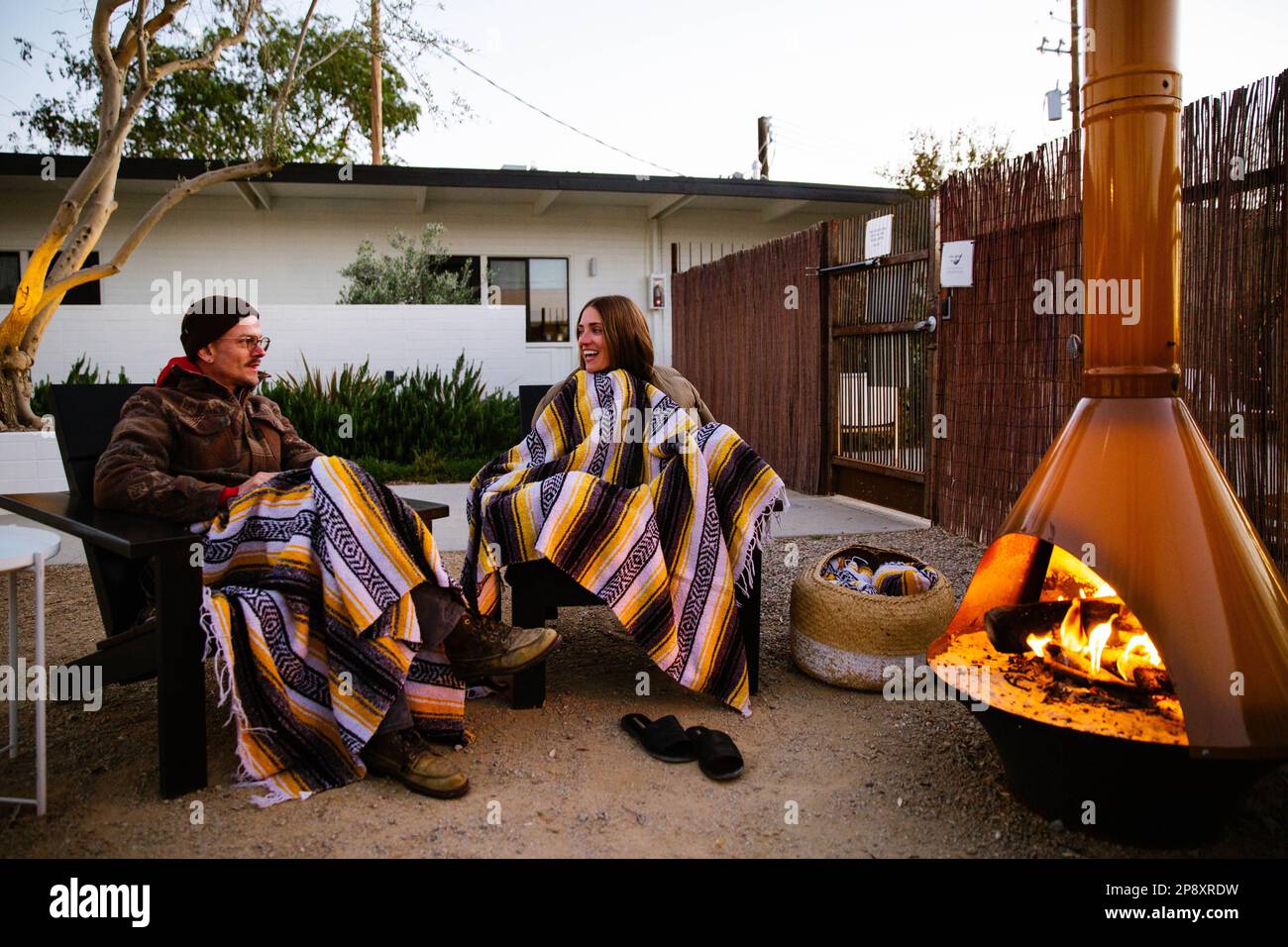 A couple sit outside at dusk and enjoy a fire in the chiminea in the courtyard of a roadside motel in the high desert. Stock Photo