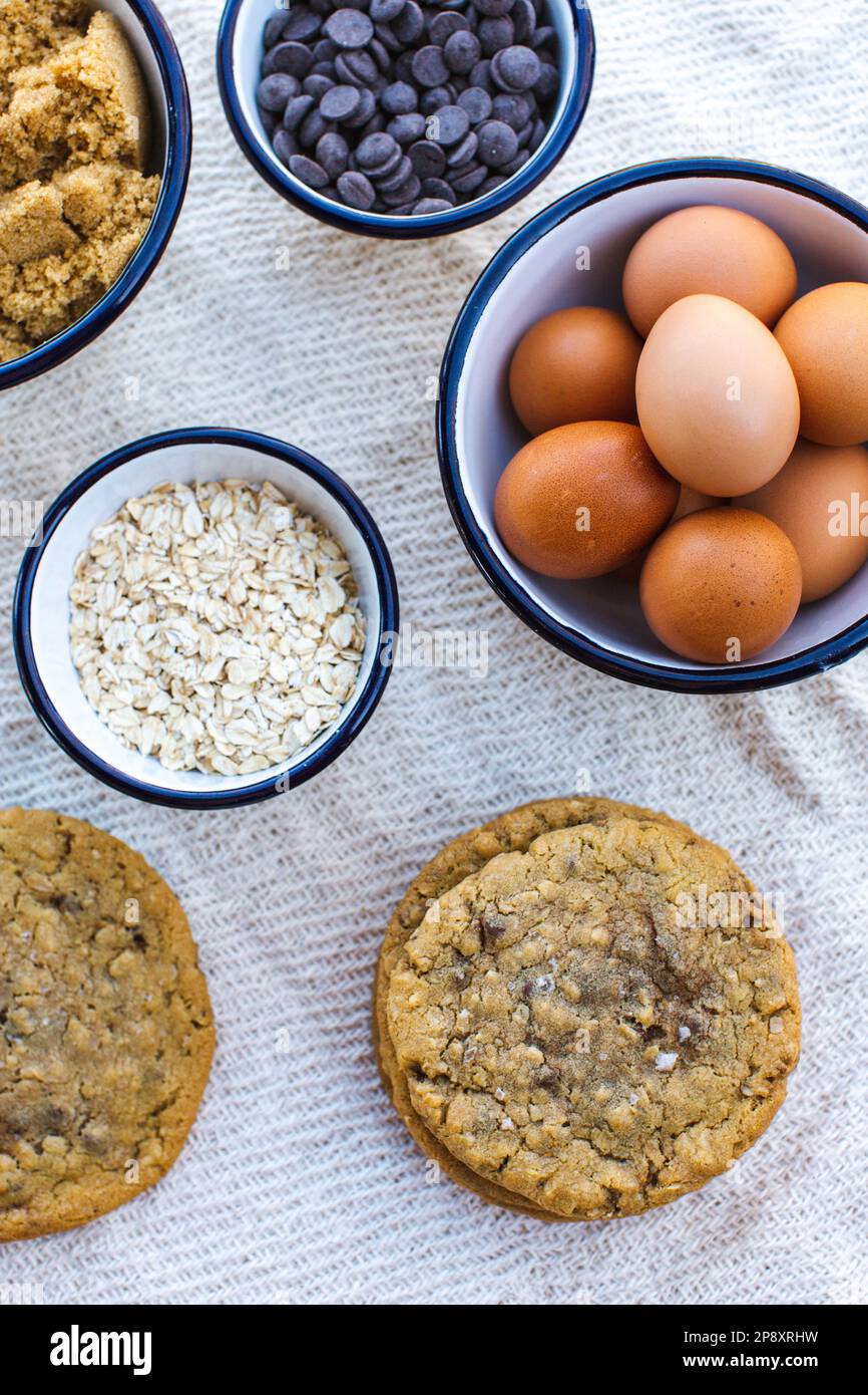 Chocolate chip cookies laid out with enamel bowls filled with the recipe ingredients. Eggs, flour, sugar, chocolate. Stock Photo