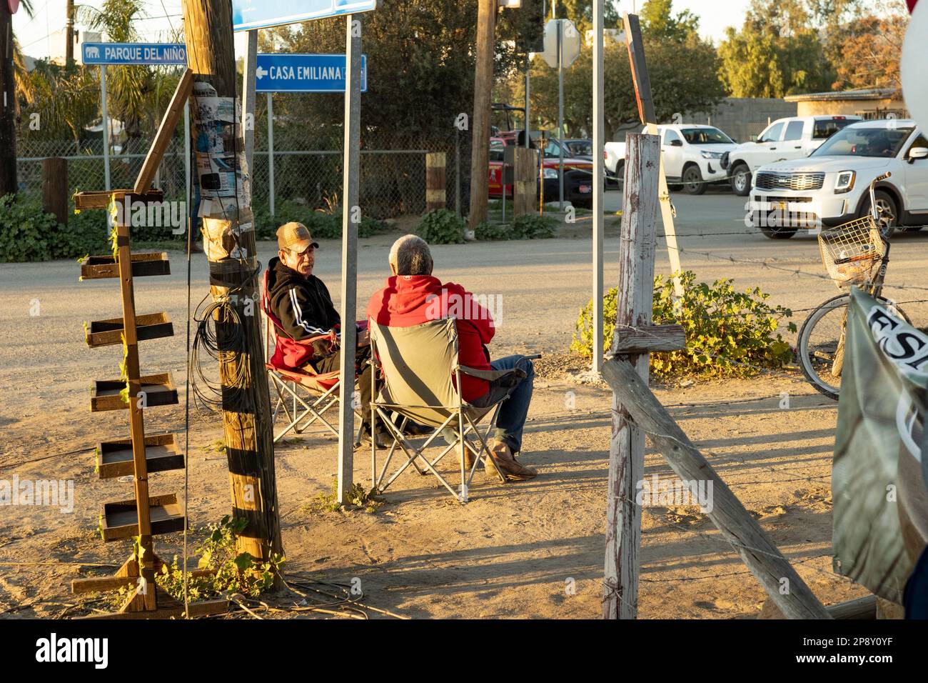 Ejido El Porvenir/Guadalupe, Baja California, Mexico - Two local men in chairs talking at intersection of Zapata and Fifth Street Stock Photo