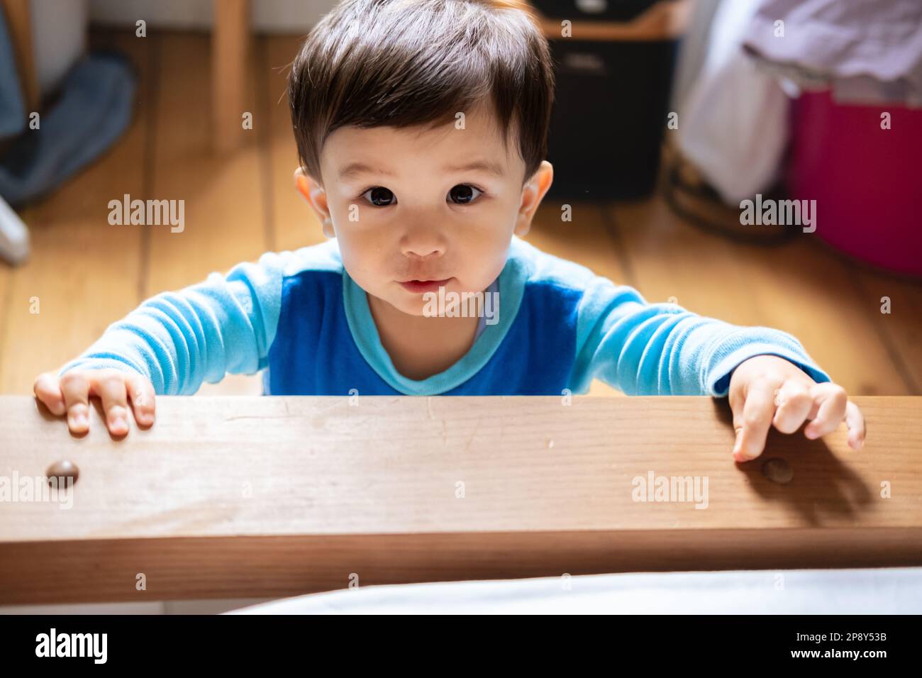 A multiracial Malaysian and Spanish baby wearing blue pajamas staring into the camera with mucus under his nose because he is sick and unwell. Touchin Stock Photo