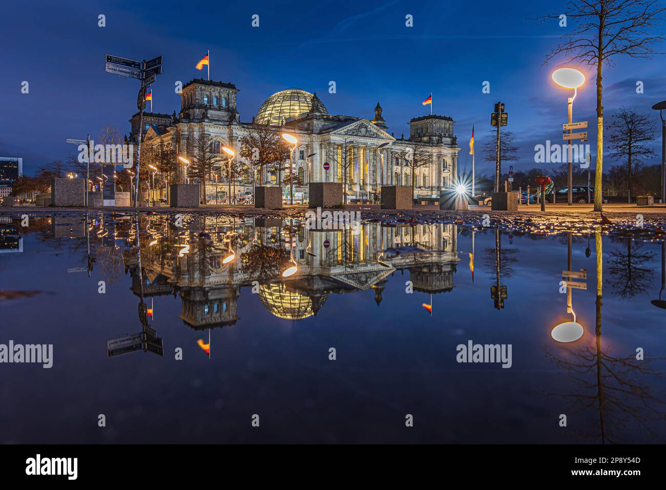 Reichstag in Berlin at the blue hour. Illuminated buildings and street lamps in the evening. Reflection of building on water surface. Evening mood Stock Photo