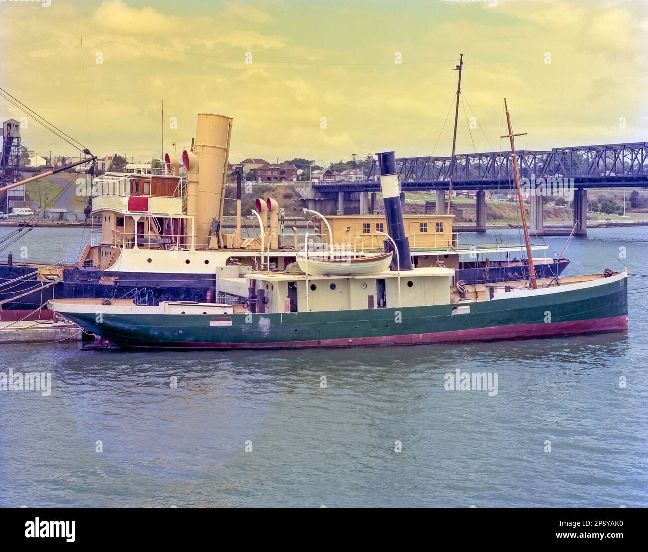 A 1981 historic image of the 1927 launched, SS John Oxley, a coal and later oil fired steamer used by the Queensland Government to support lighthouses and act as a pilot boat. She was donated to the Sydney Heritage Fleet in 1970 and moored here at Birkenhead Point until a full 20 year restoration began in 2002. In the foreground is the coal-fired steam tug Waratah, also in a pre-restoration state and missing its wheelhouse. In the background is the old Iron Cove Bridge shown 30 years before the second bridge was opened in 2011 Stock Photo