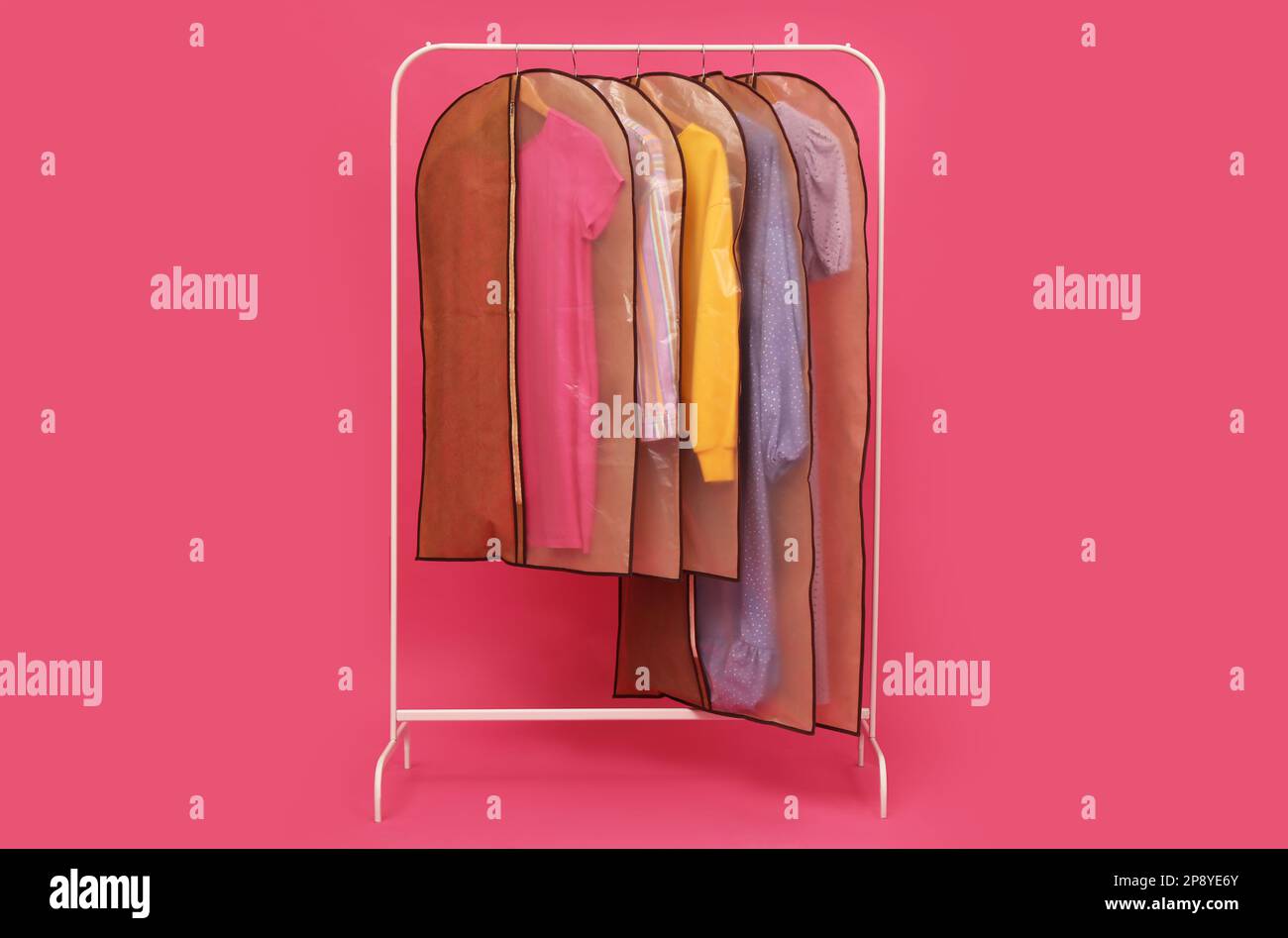 Garment bags with clothes on rack against pink background Stock Photo ...