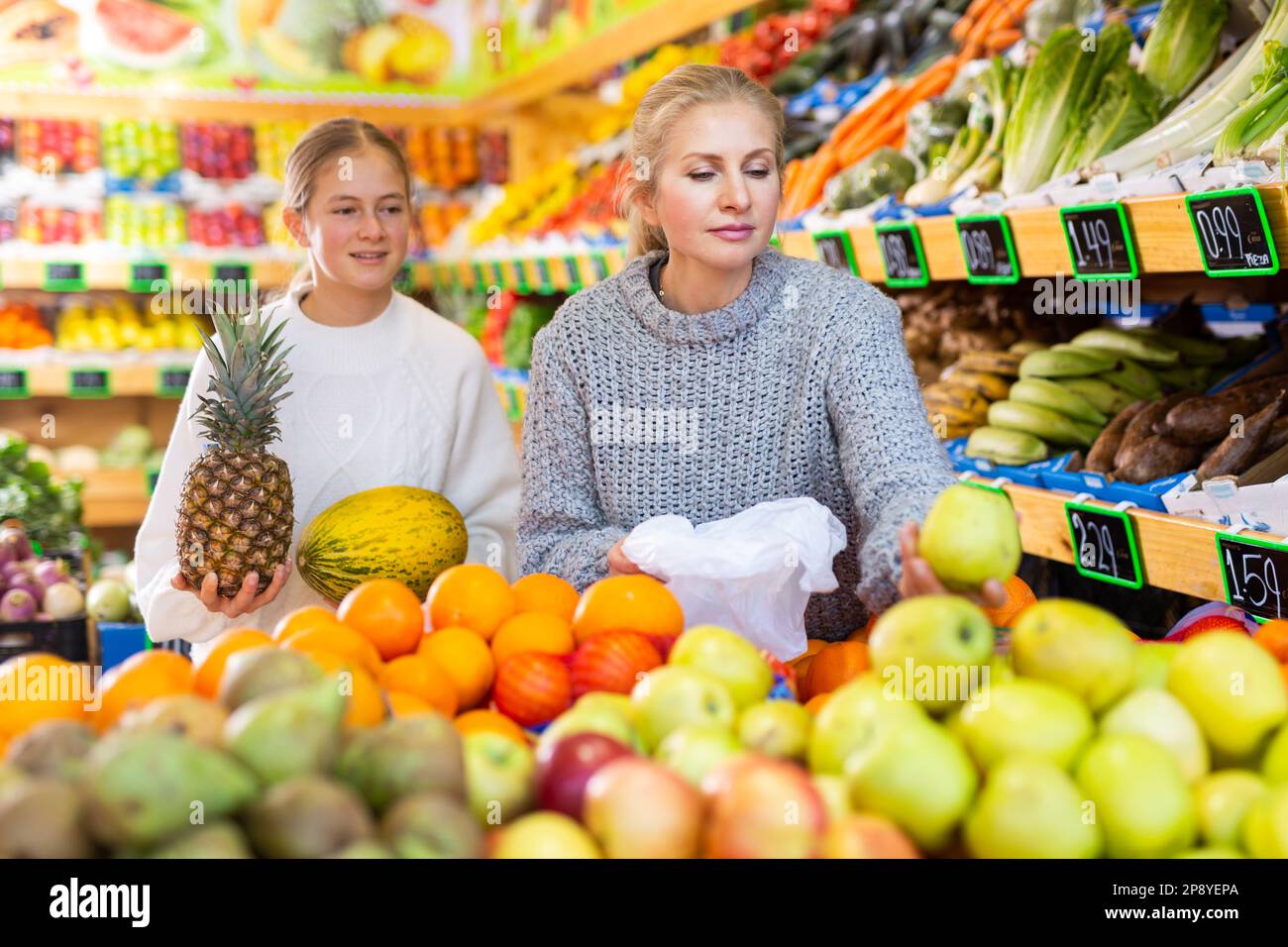 Smiling teenage girl with mother choosing fruits and vegetables in ...