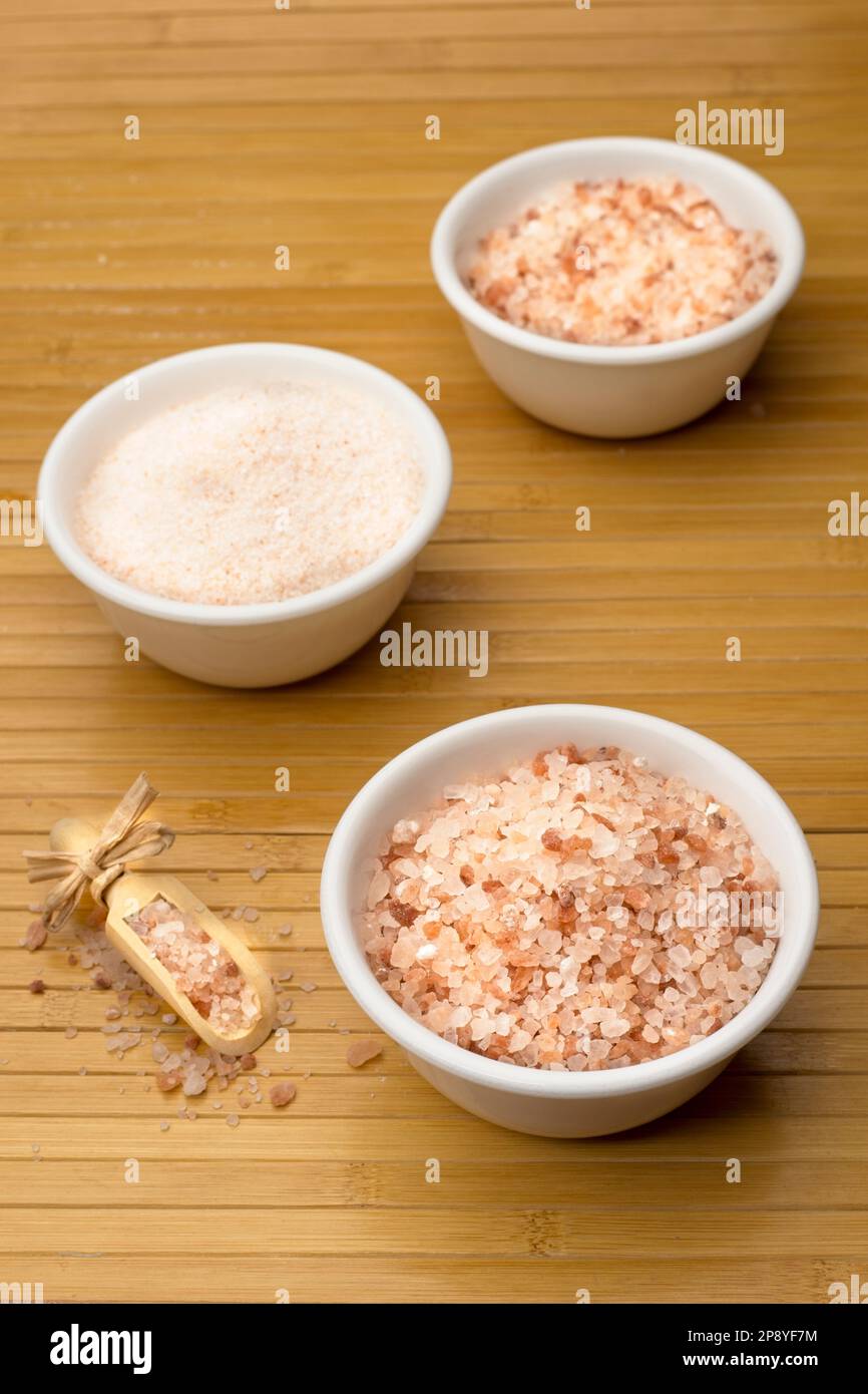 A close up studio photo of coarse and fine grain pink himalayan sea salt with a wooden scoop on the side. Stock Photo
