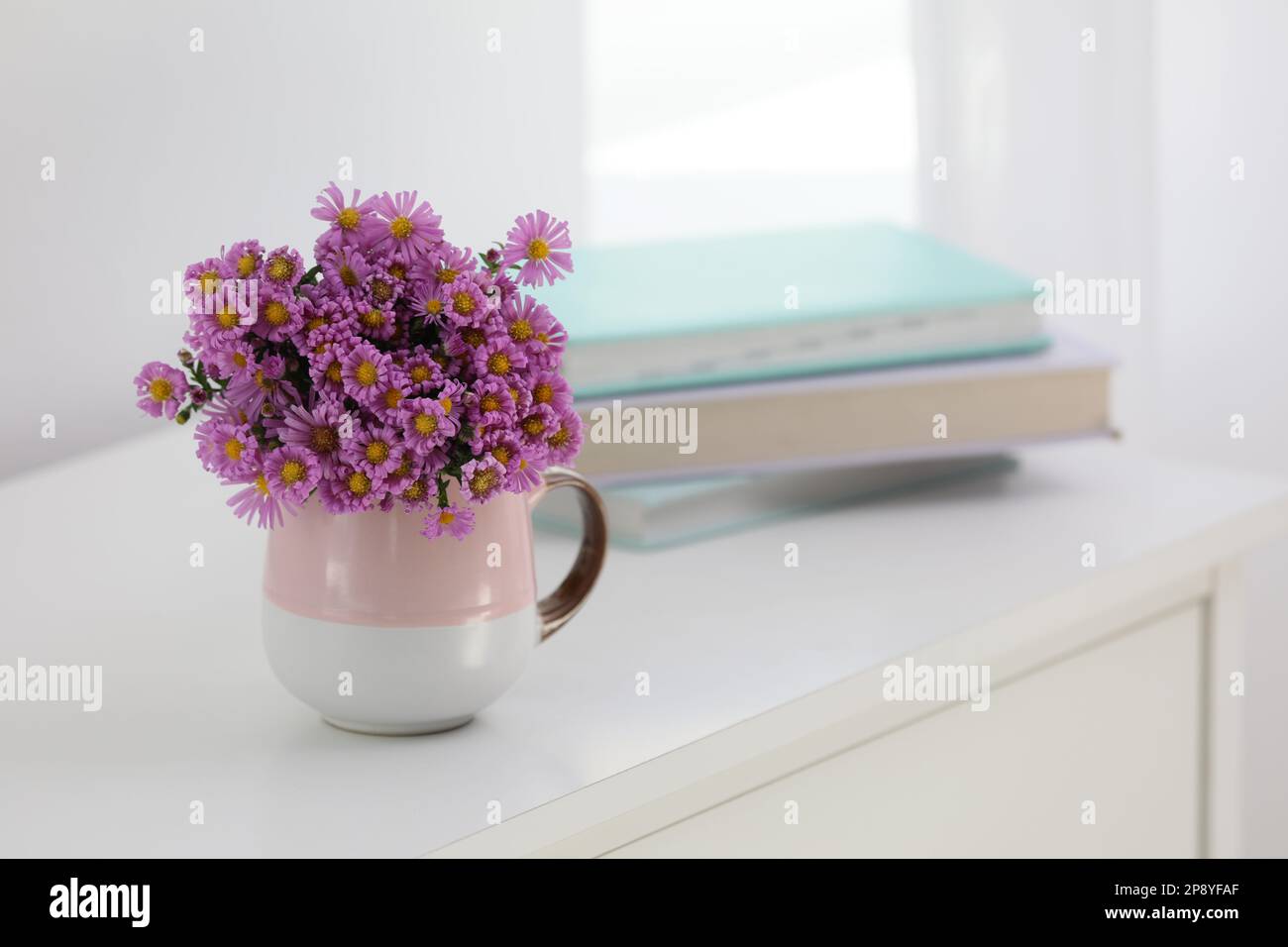 Cup with beautiful flowers on white table in light room. Space for text Stock Photo