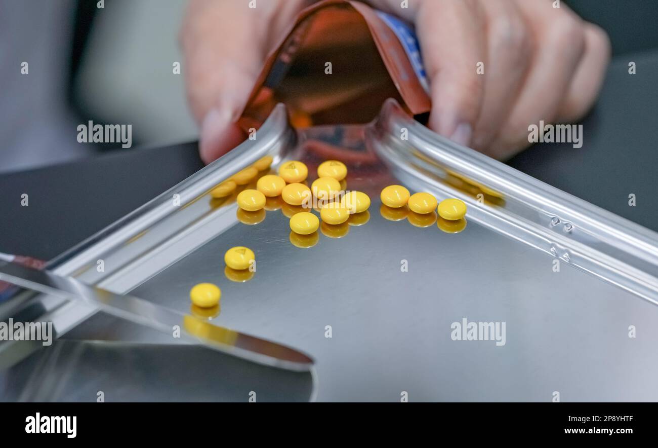 Selective focus on yellow tablets pills on stainless tray with blur hand of pharmacist or pharmacy technician counting pills into a plastic zipper bag Stock Photo