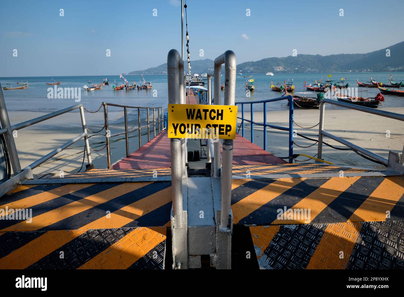 'Watch Your Step' warning sign at the pier of Patong, Patong Beach, Patong Bay, Phuket, Thailand, so-called longtail boats anchored in the background Stock Photo