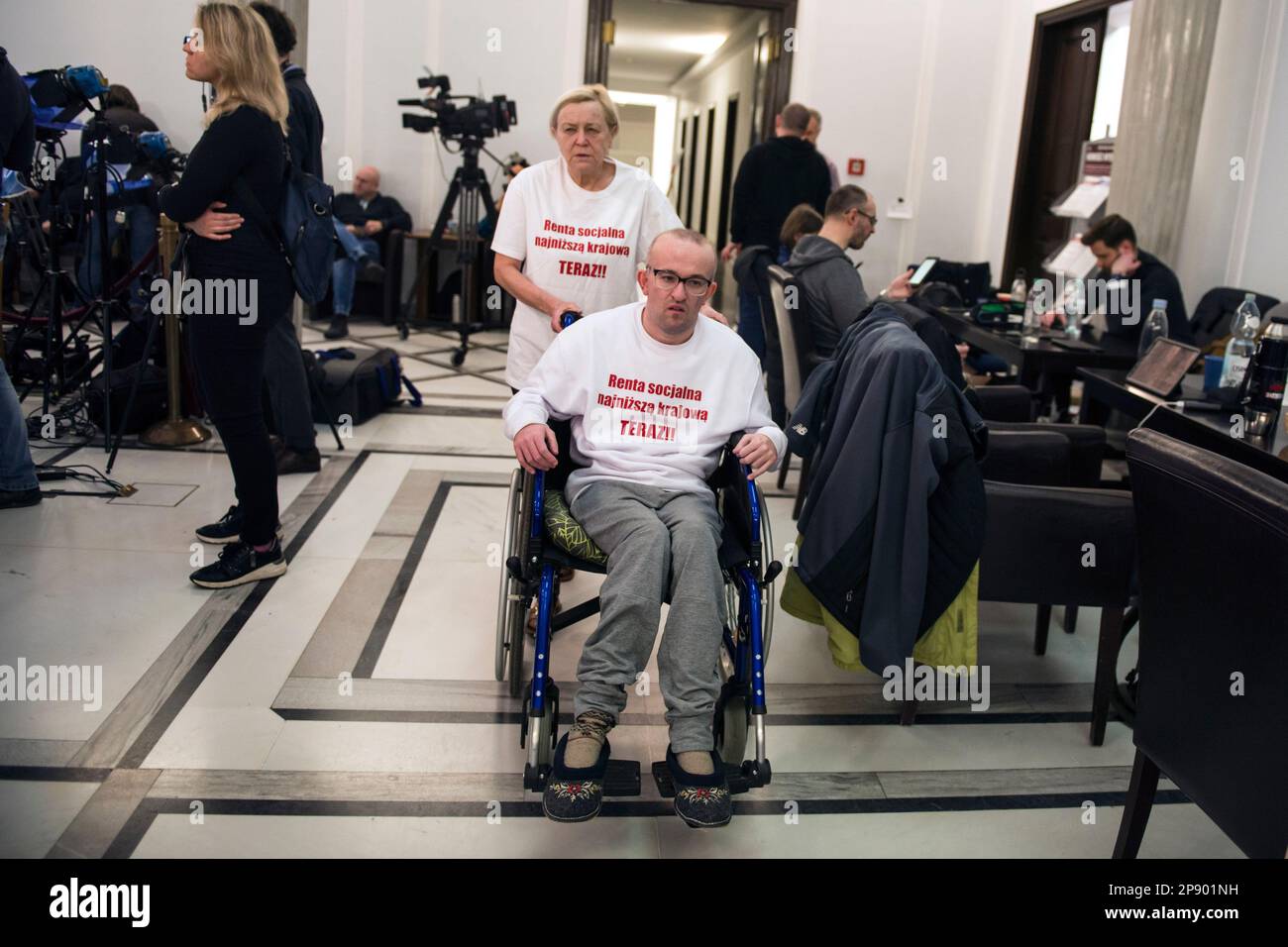 A mother of differently abled man named Andrzej Sucholewski is pushing his wheelchair at the Parliamentary corridor. It is the 4th day since a group of Persons with disabilities along with their parents and care takers gathered in the Sejm (lower house of Parliament) on Monday 6th of March, demanding that the social pension be equalized with the national minimum. Among the protesters in the Sejm is also MP - Iwona Hartwich with her disabled son, Jakub. The PO's (Civic Platform) MP informed during a press conference that people with disabilities are submitting a draft act on social pension, aft Stock Photo