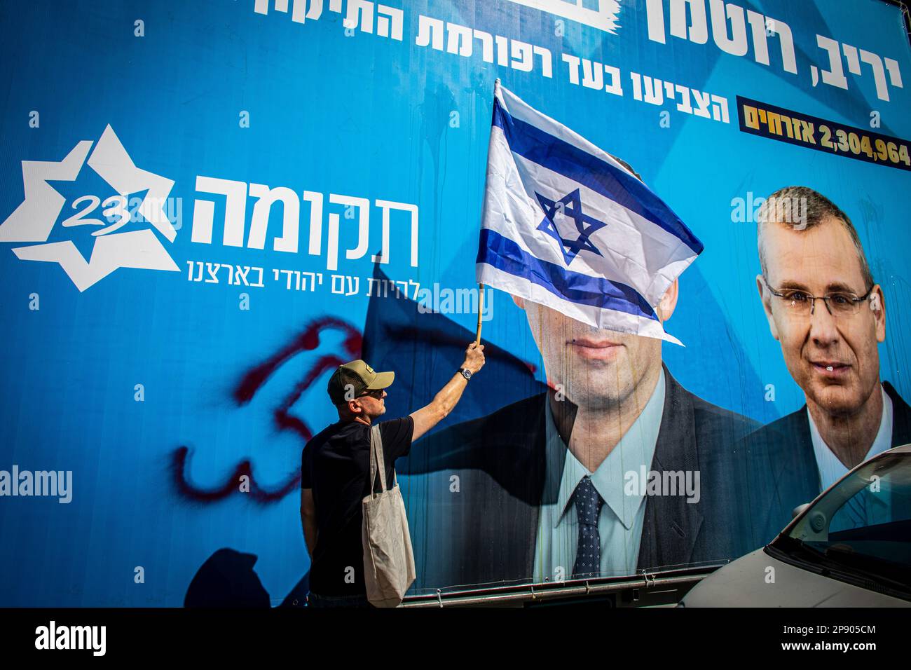 Tel Aviv, Israel. 09th Mar, 2023. A protestor waves the Israeli flag in front of a poster showing Knesset member and chairman of the judicial commits and Minister of justice Yariv Levin (R) during a demonstration. Tens of thousands of protesters marched in Tel Aviv as a 'day of resistance' against the government's judicial overhaul plans. They blocked the Tel Aviv Ayalon Highway, to stop the traffic to critical industrial and high-tech areas throughout the capital. Credit: SOPA Images Limited/Alamy Live News Stock Photo