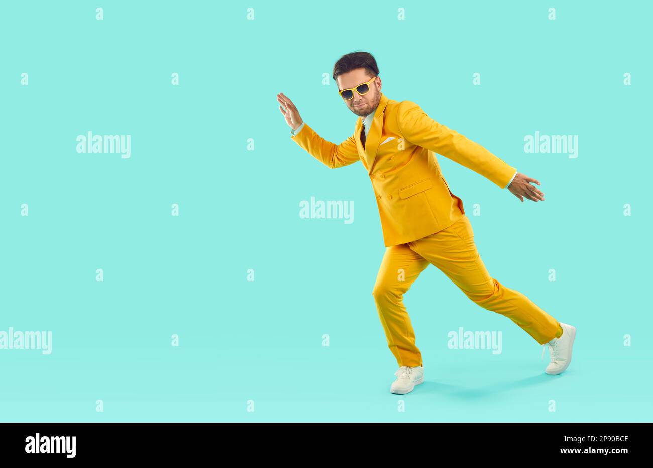 Confident man in a yellow suit dancing or walking in a funny way on a blue studio background Stock Photo