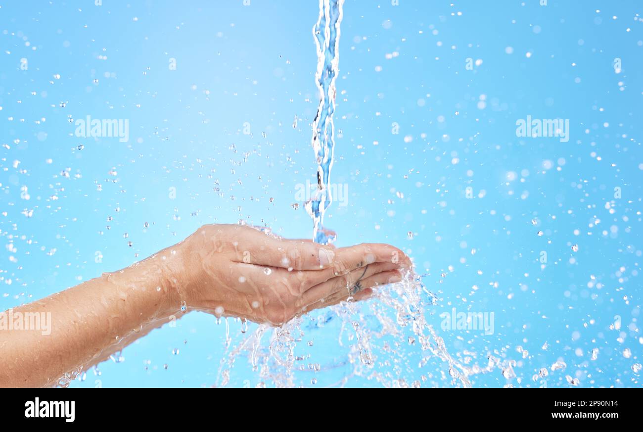 Hand, water and cleaning with a splash in studio on a blue background ...