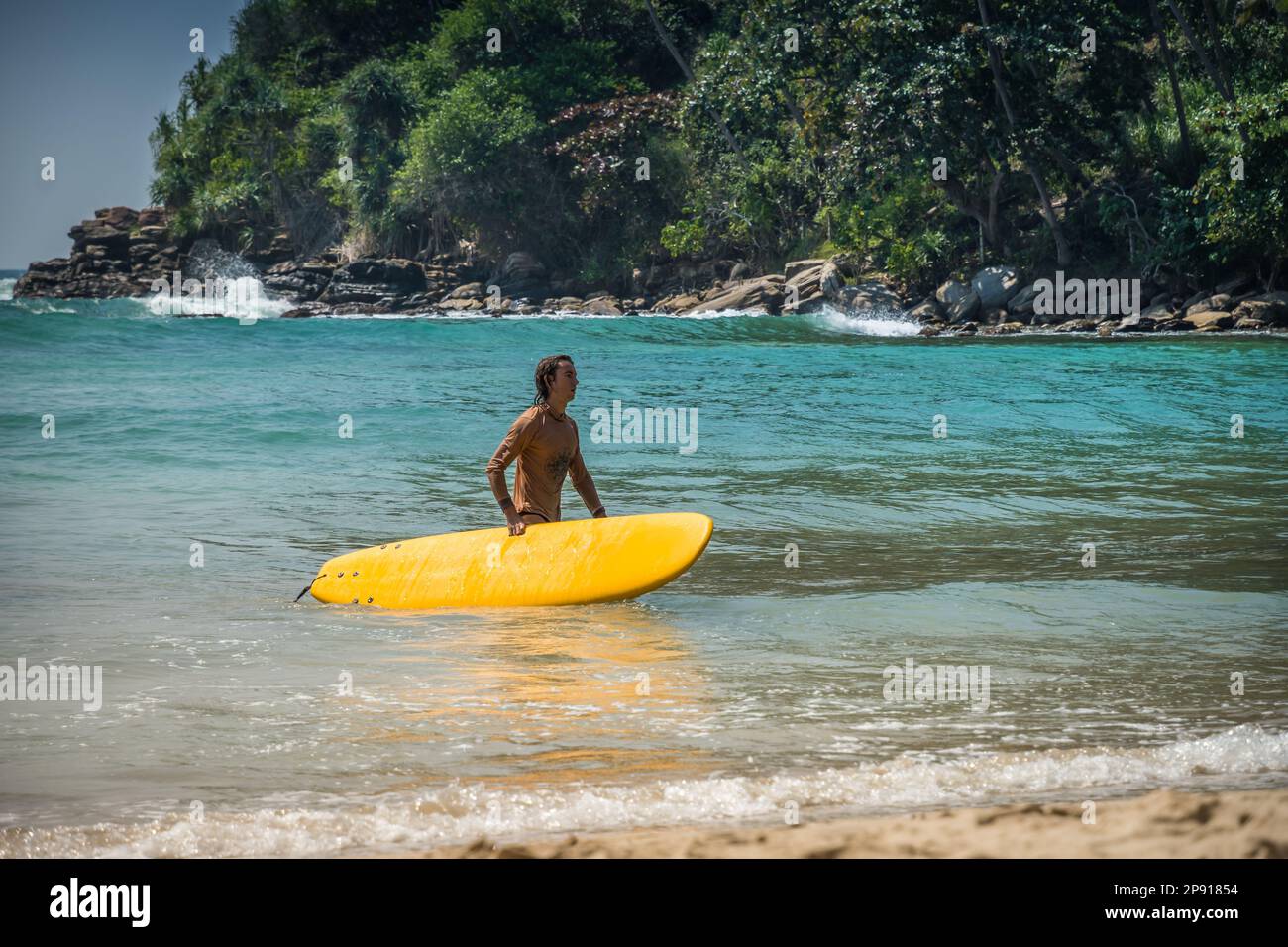 Hiriketiya Beach, Dickwella. Sri Lanka - 16.02.2023. Young caucasian guy goes out with surfboard on ocean shore after surfing. Tropical vacation on Sr Stock Photo