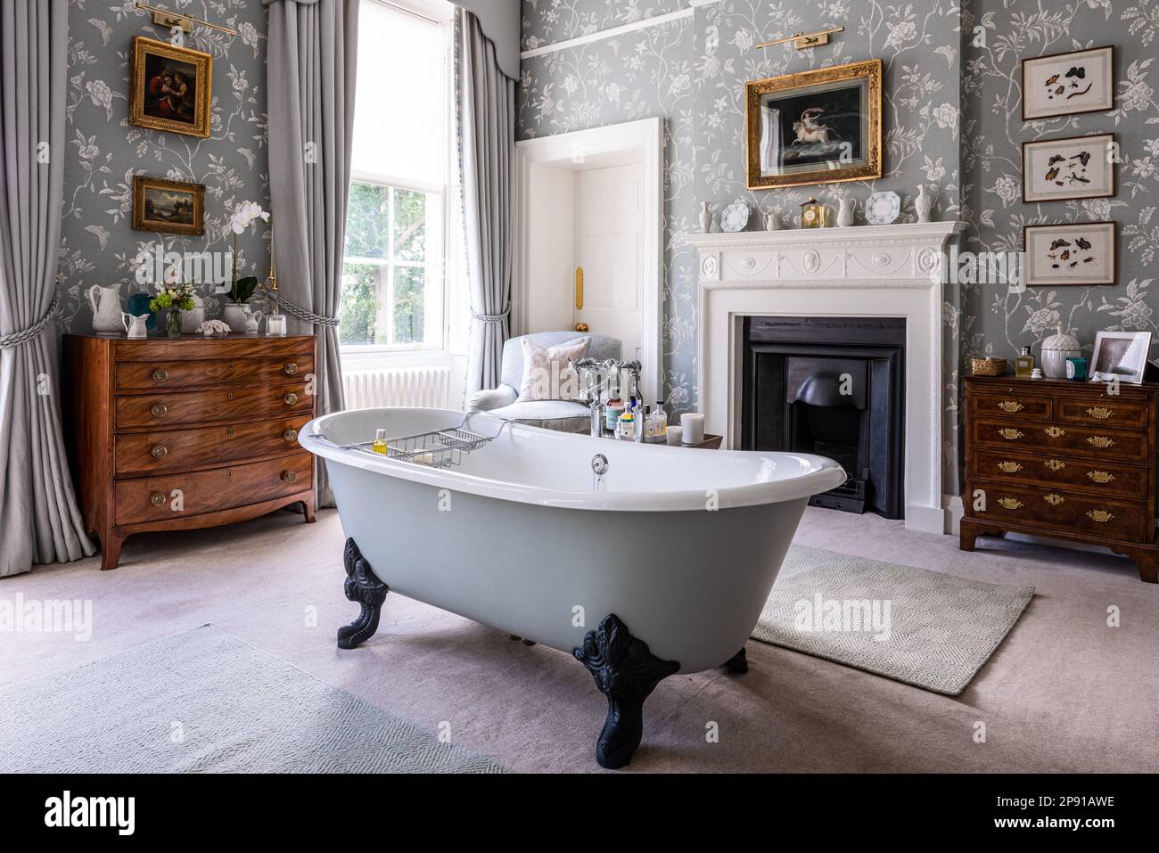 18th century chests with Colefax and Fowler wallpaper and cast iron bath in Grade II listed Suffolk country house, UK Stock Photo