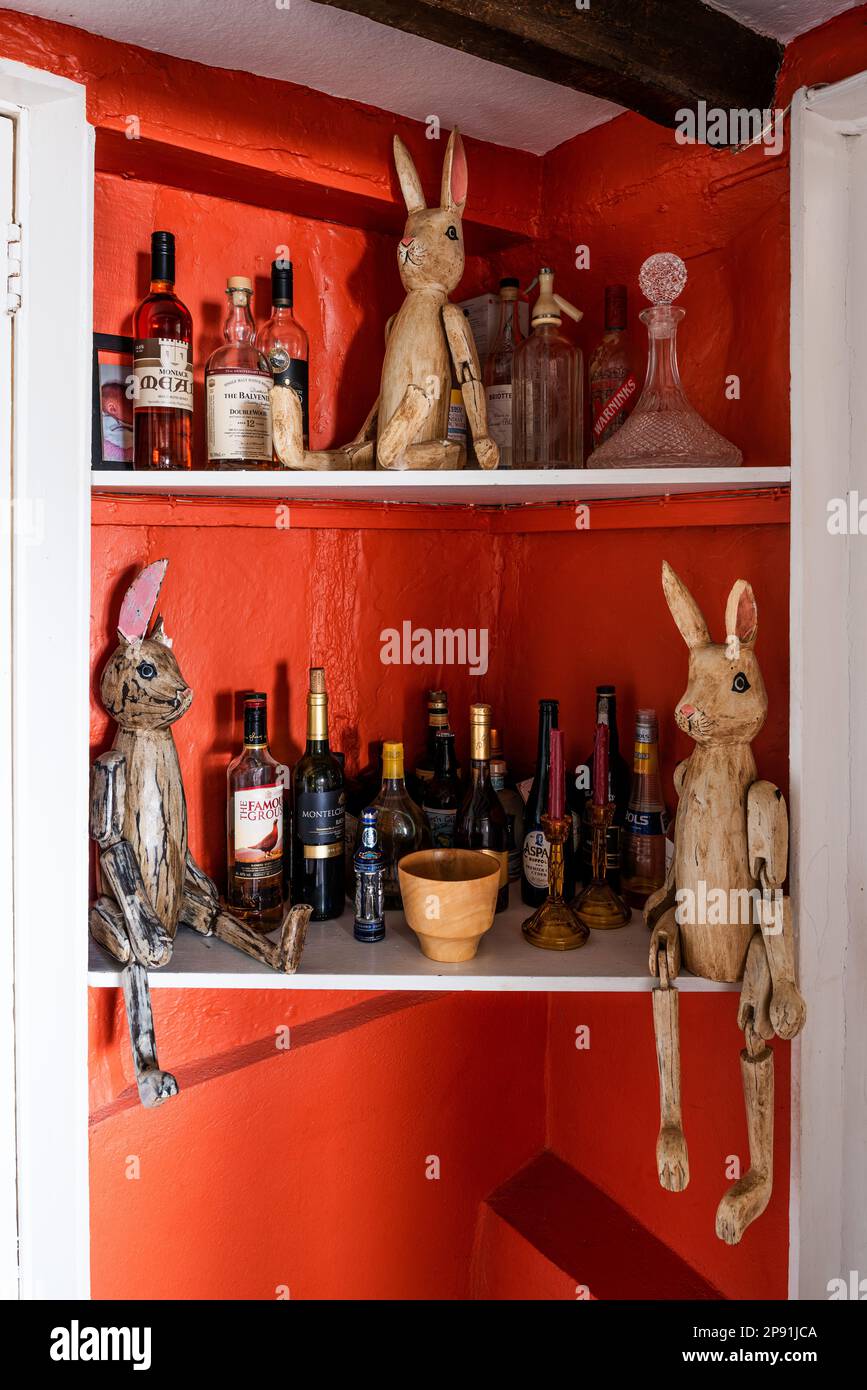 Articulated bunnies and alcohol in shelf space with walls painted in 'Cornflower Locks'. 16th century Tudor farmhouse, Suffolk, UK. Stock Photo