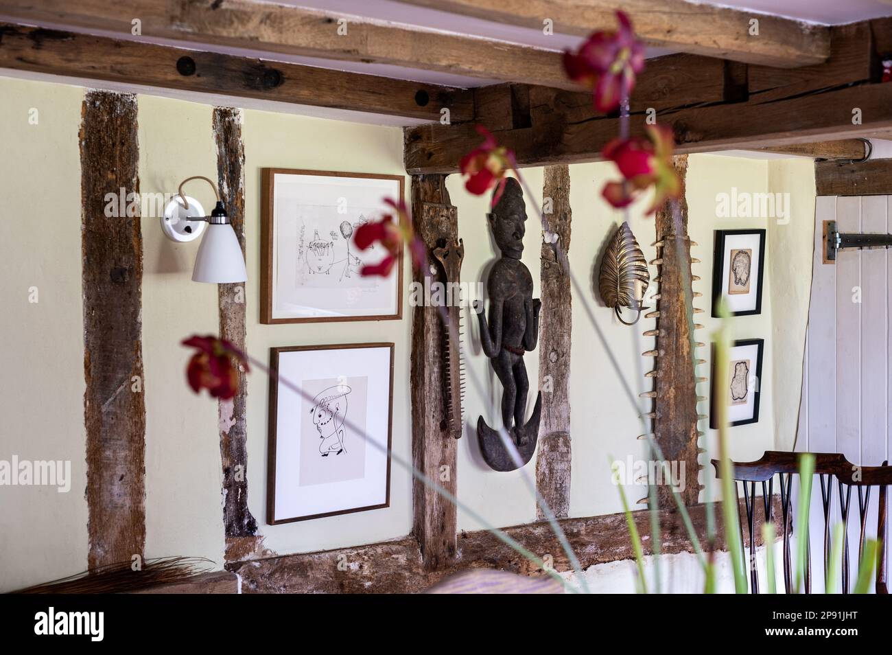 African sculpture with framed prints and orchid in 16th century Tudor farmhouse, Suffolk, UK. Stock Photo