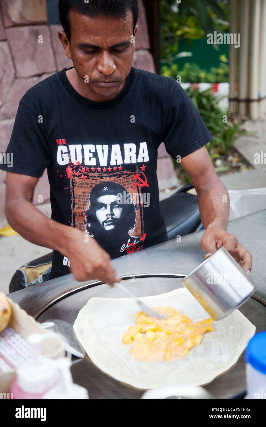 Pattaya, Thailand - March 22, 2016: Indian man cooking a crepe stuffed with mango on a street food cart in Thailand, wearing Che Guevara T-shirt Stock Photo