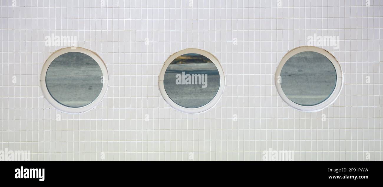 3 round mirror windows in a row on a white tiled building wall background Stock Photo