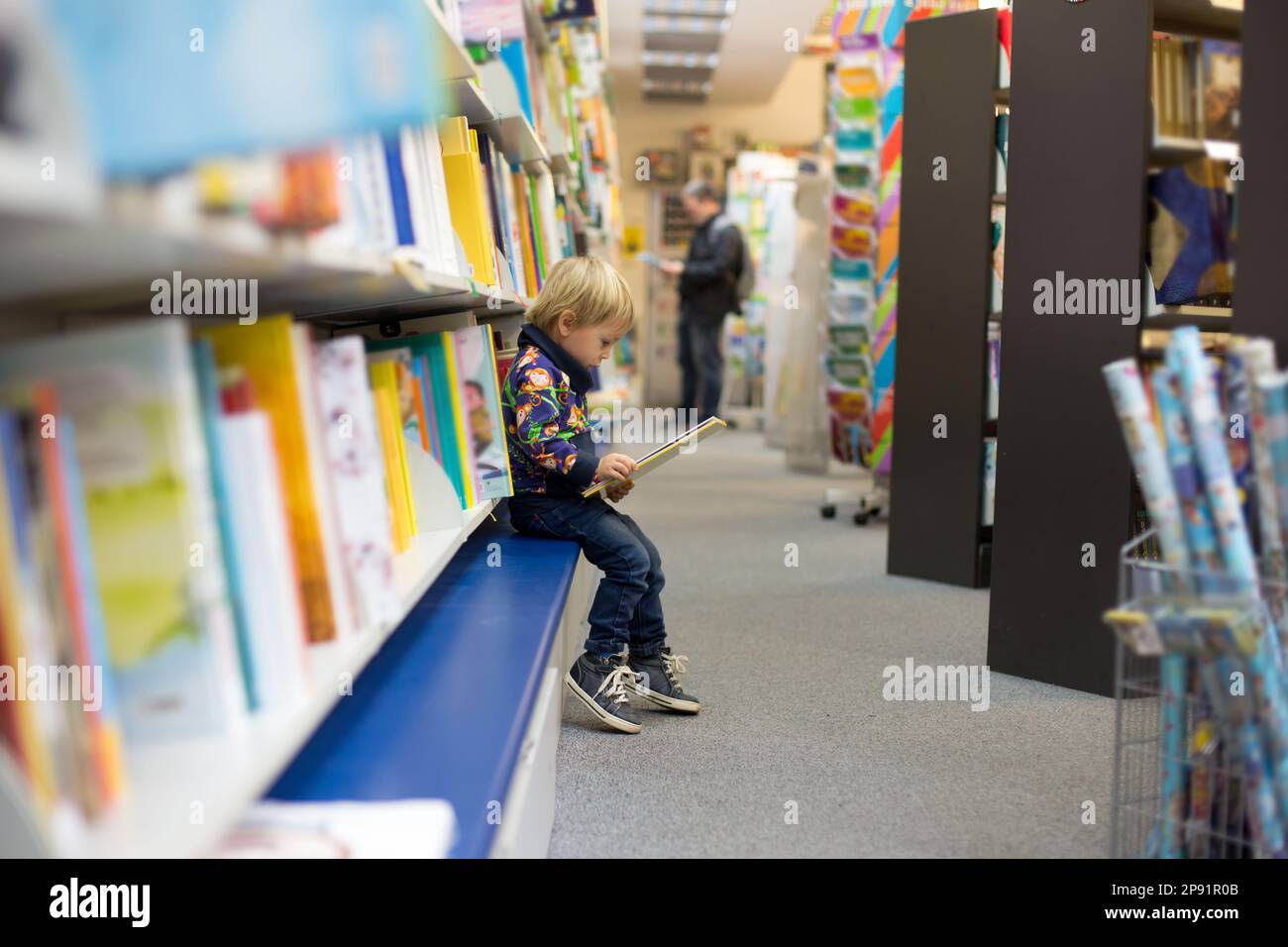 Adorable little boy, sitting in a book store and read book Stock Photo ...