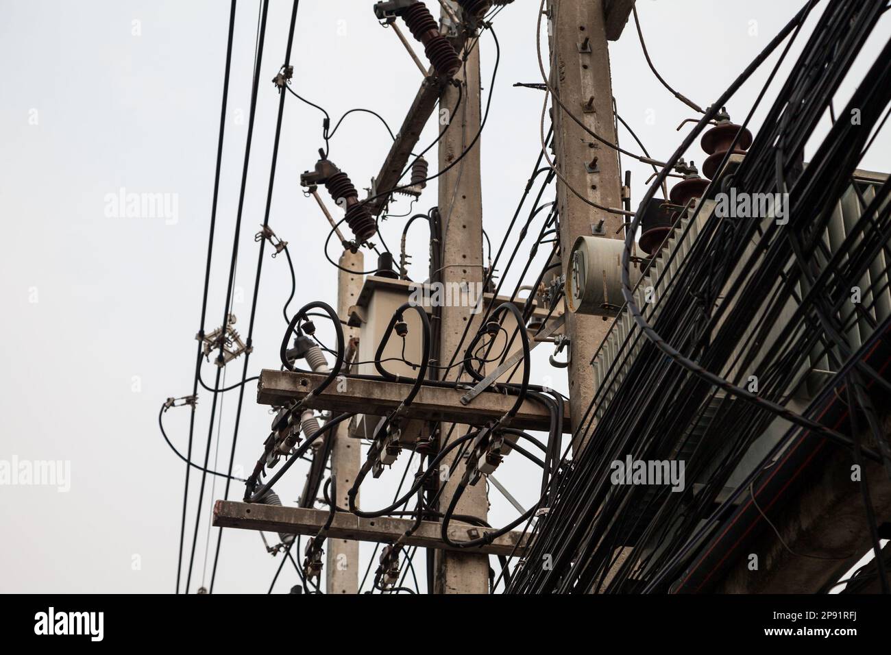 Few utility poles, complicated wires and a lot of telephone cables against the gray sky. Many chaotic electric and phone cables in a Thai city Stock Photo