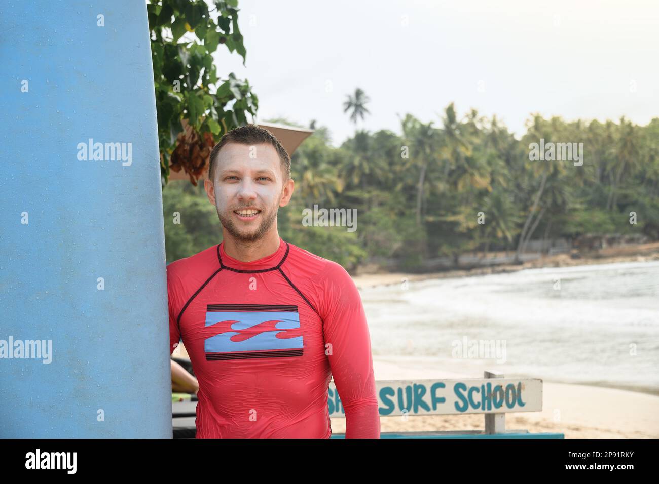Surfer with special natural sunblock zink on his face holding his surfboard and waiting big waves for surfing. Copy space. Tropical vacation on Sri La Stock Photo