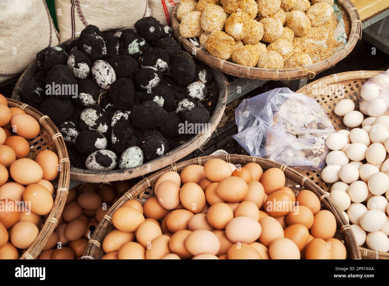 Several baskets of raw and cooked eggs at Vietnamese market. Pile of Asian delicacy black century eggs in ash Stock Photo