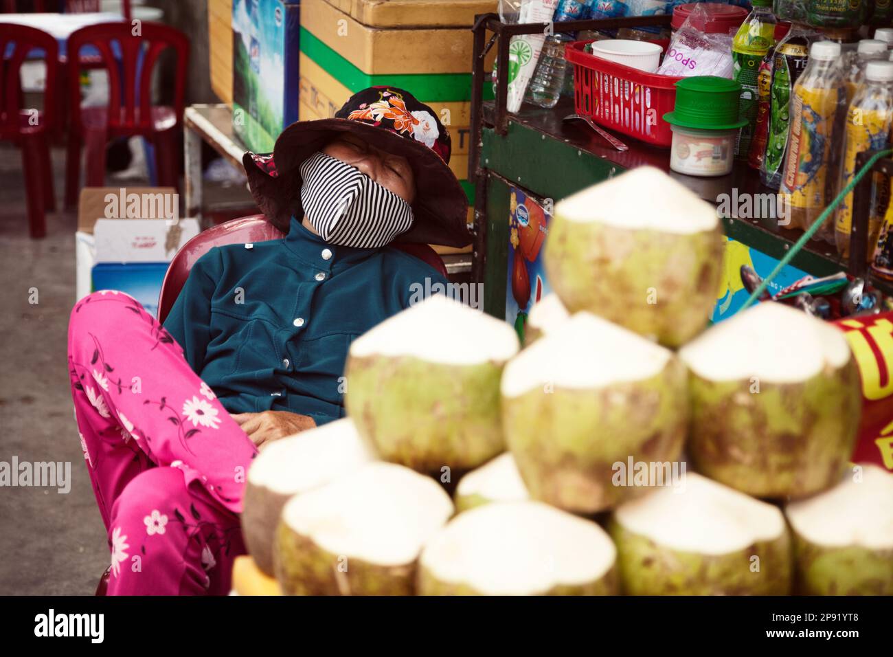 Nha Trang, Vietnam - April 1, 2018: Vietnamese street food vendor sleeping at a workplace. Tired Asian lady selling coconuts at a market Stock Photo