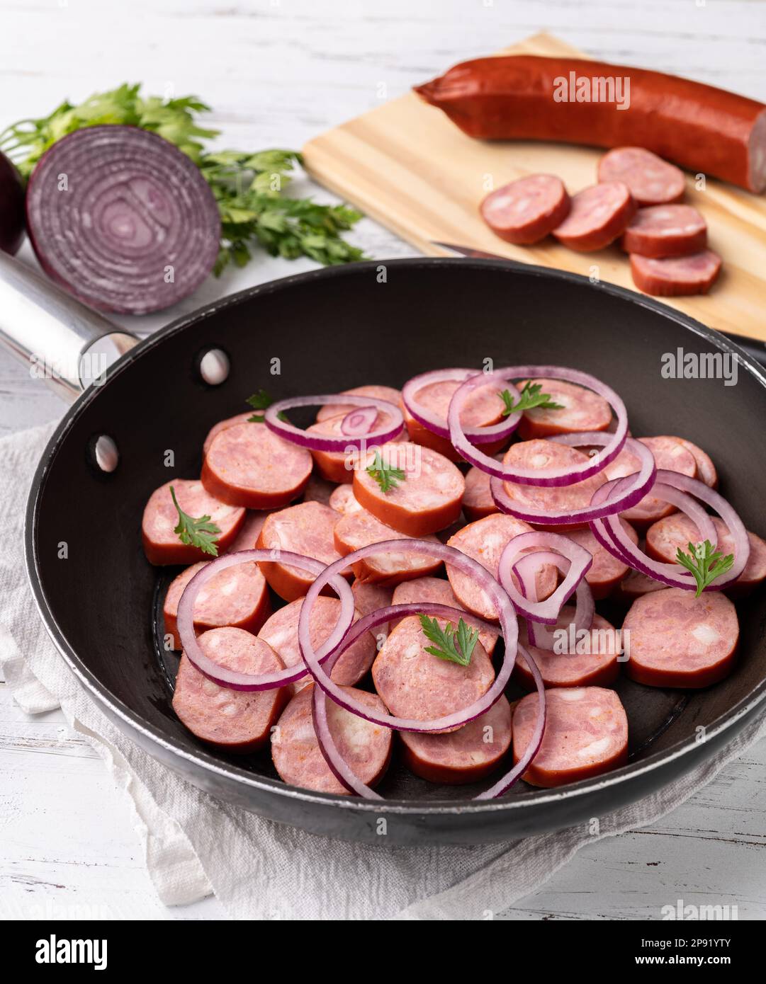 Uncooked calabrese sausage slices in a pan with onion, pepper and herbs over white wooden table. Stock Photo