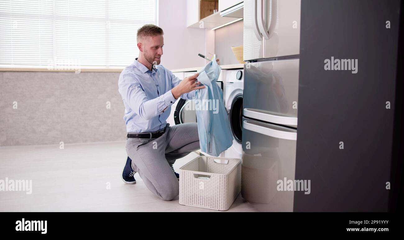 Young Man Loading Clothes Into Washing Machine In Kitchen Stock Photo