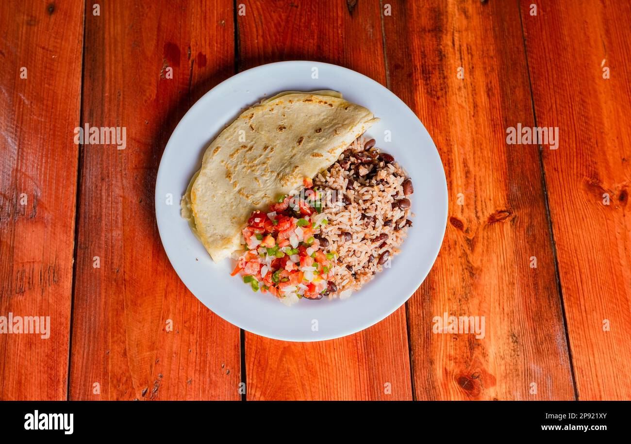 Quesillo dish with gallo pinto and pico de gallo on wooden table. Nicaraguan food Gallo pinto with pico de gallo and Quesillo served Stock Photo