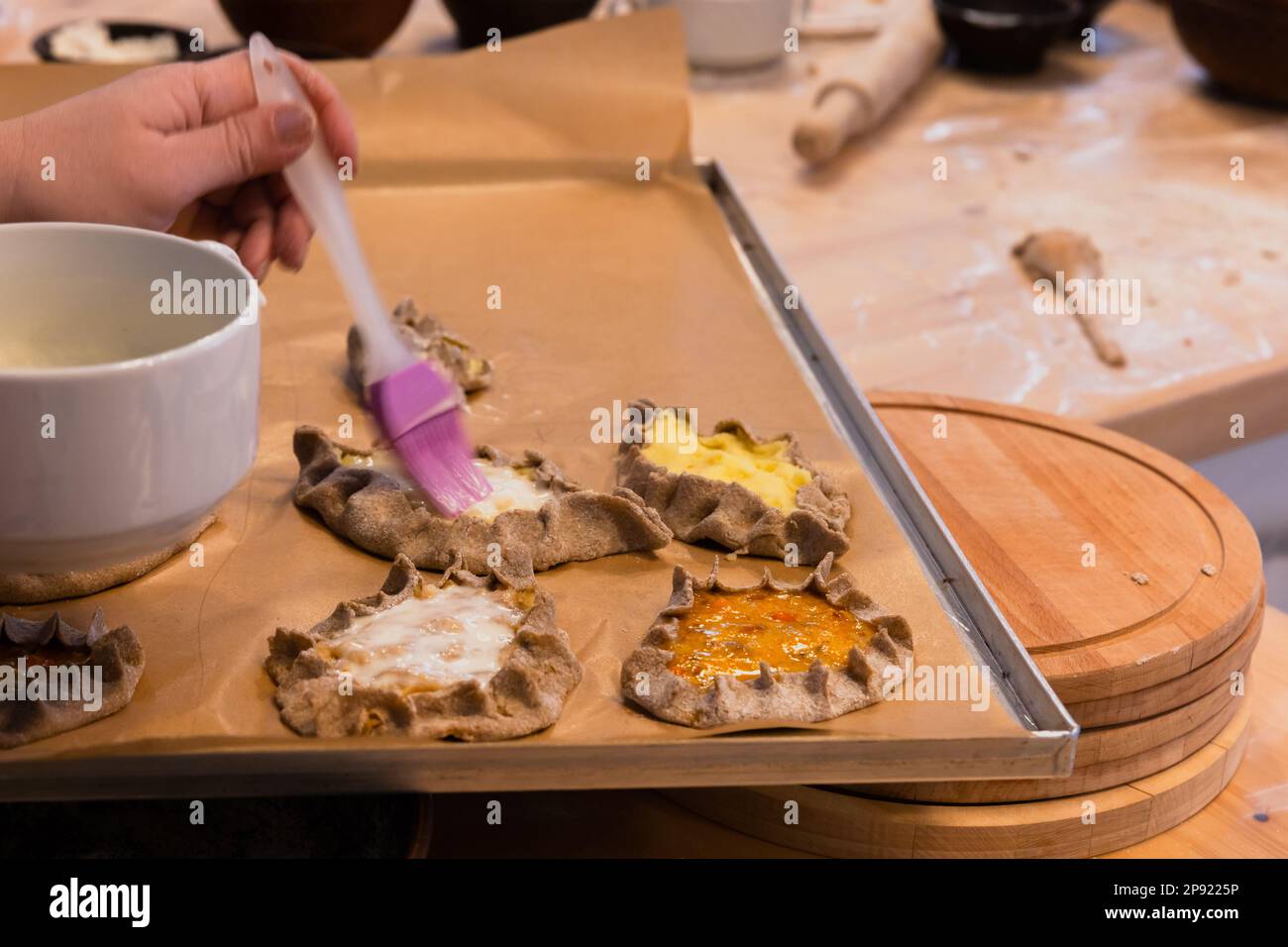 Preparing homemade Karelian pasties for bake, brushing with melted butter, close up photo with selective soft focus Stock Photo