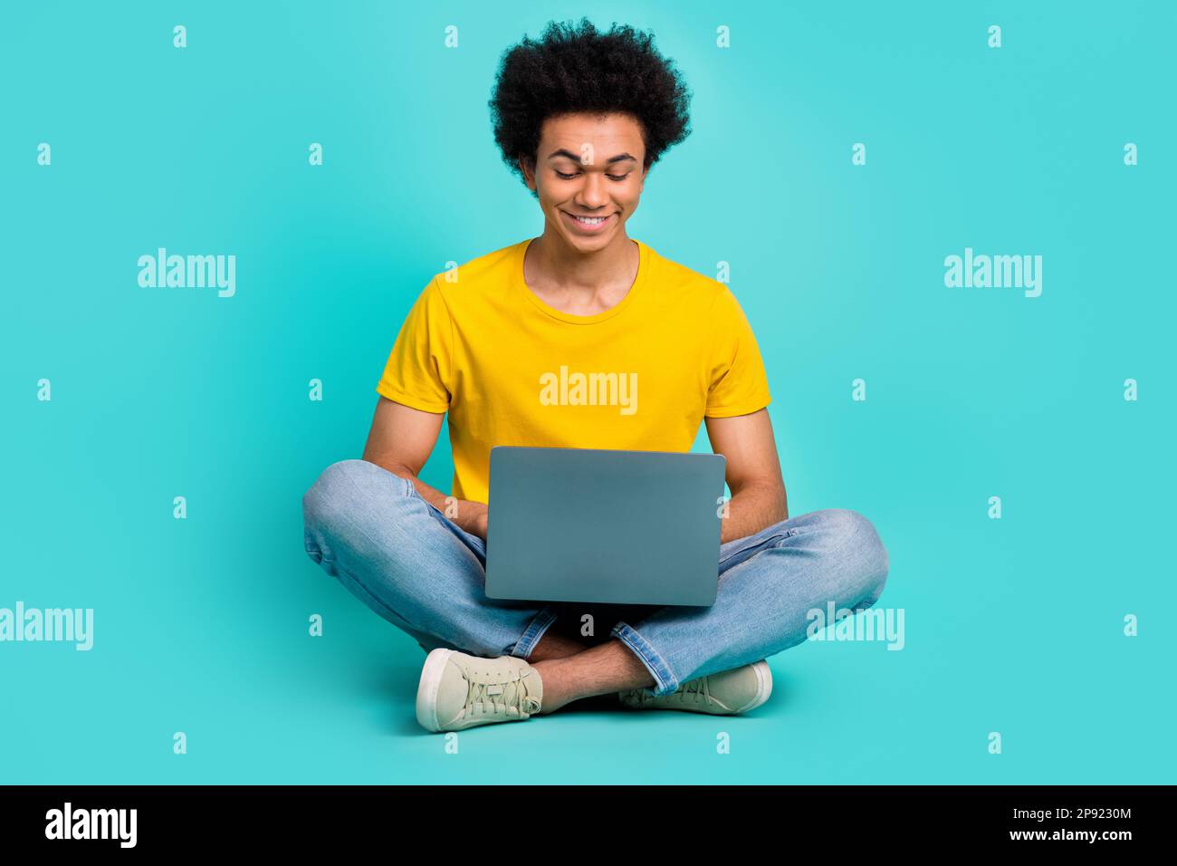 Full length portrait of cheerful nice young man sit floor use wireless netbook isolated on teal color background Stock Photo
