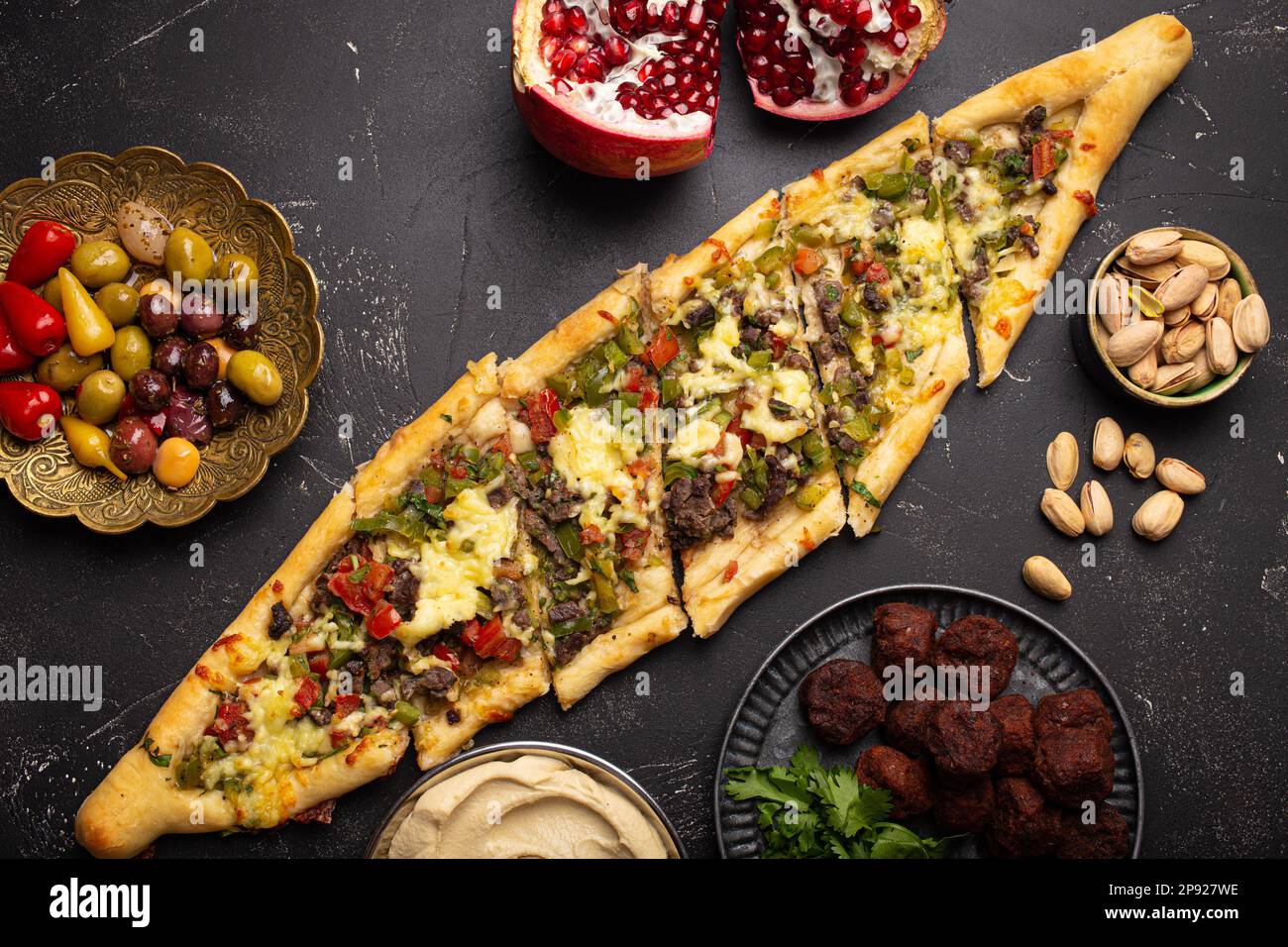 Traditional Turkish pizza pide freshly baked with ground beef and vegetables served on black stone background with assorted Middle Eastern meze from Stock Photo