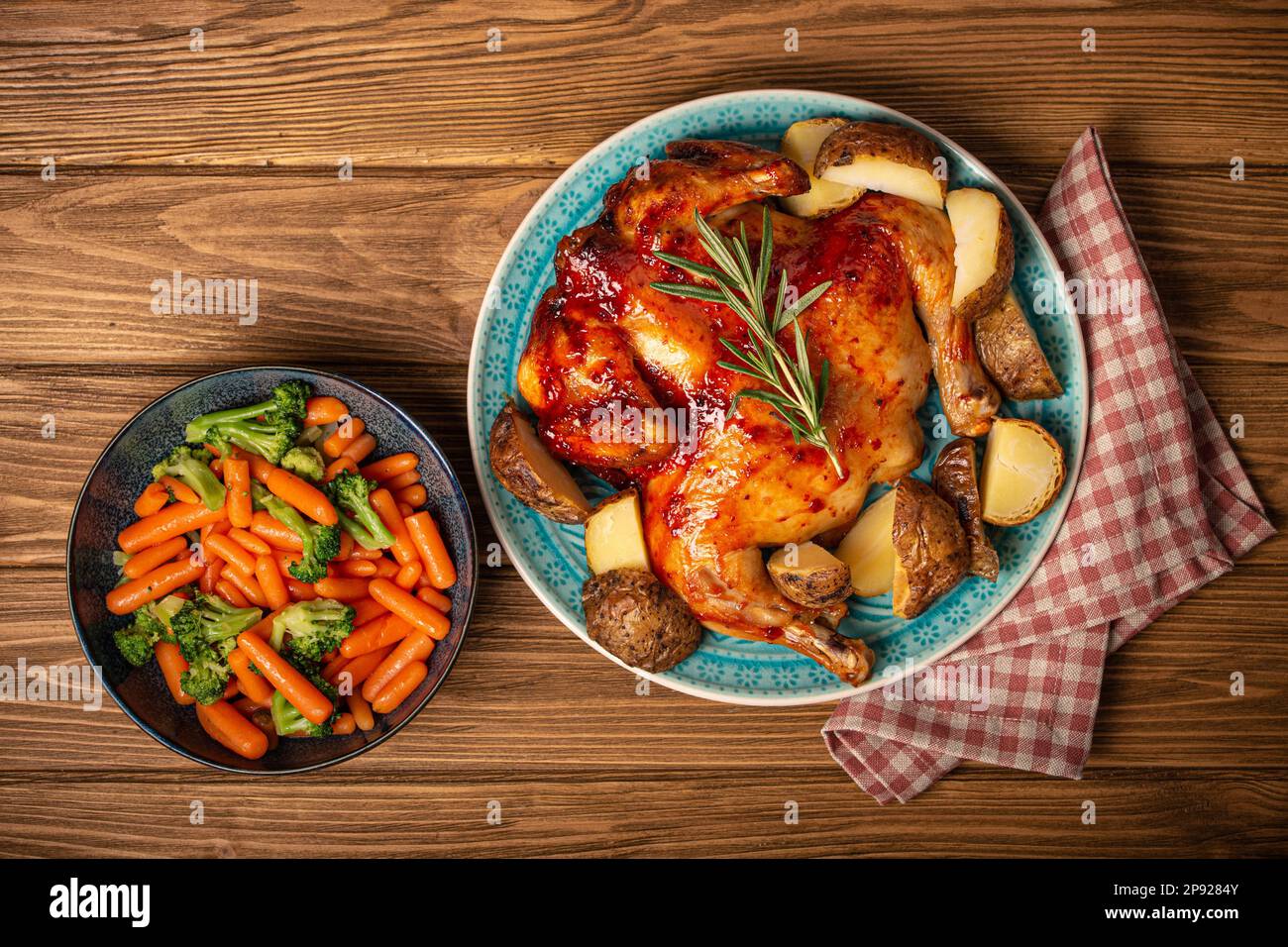 Delicious roasted whole chicken and vegetables in bowl top view on wooden rustic background top
