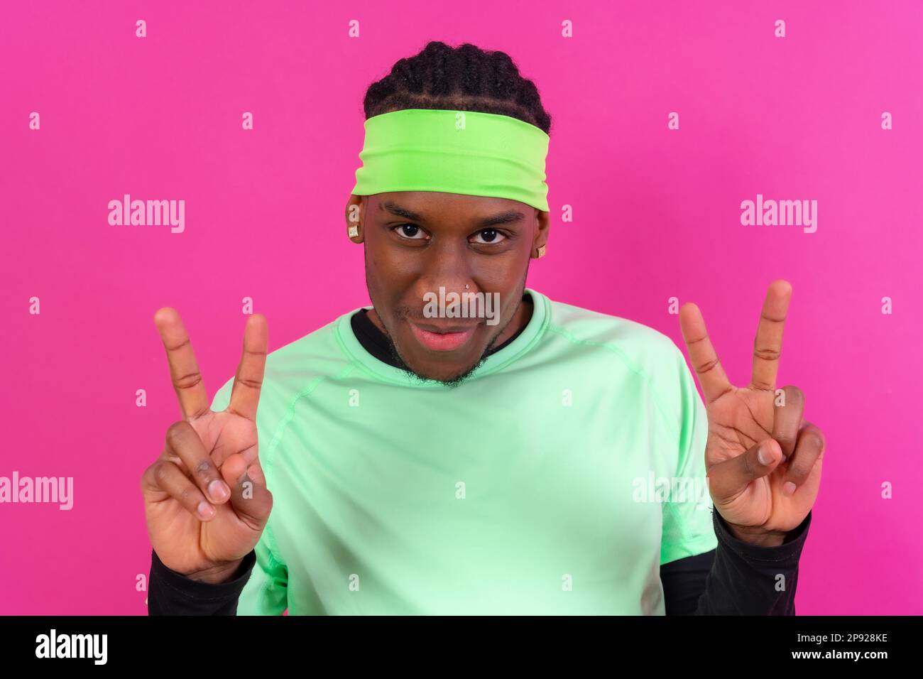 Black ethnic man in green clothes on a pink background, making the win gesture Stock Photo