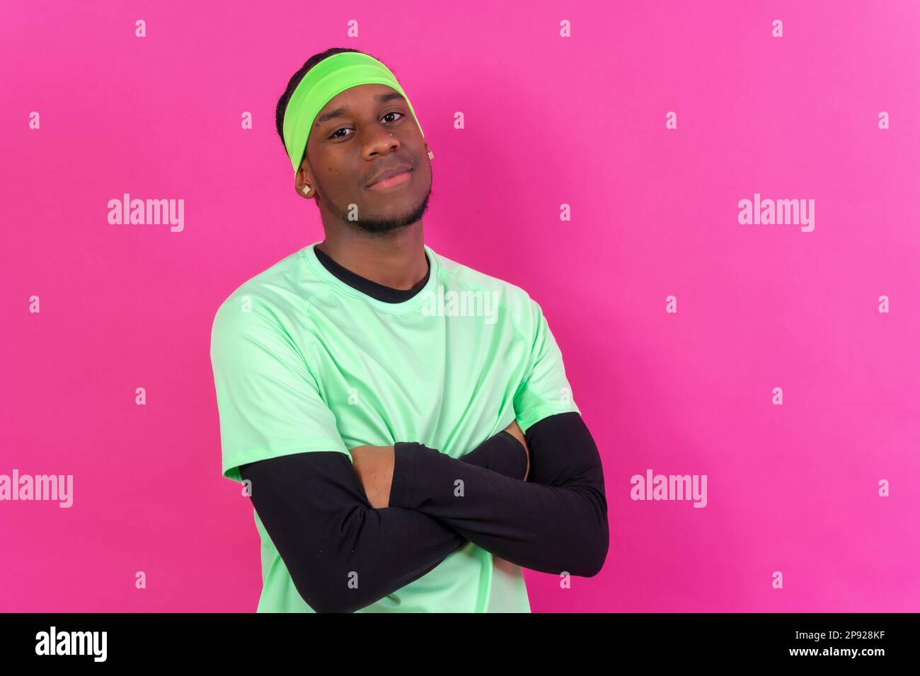 Black ethnic man in green clothes on a pink background, concept portrait, arms crossed Stock Photo
