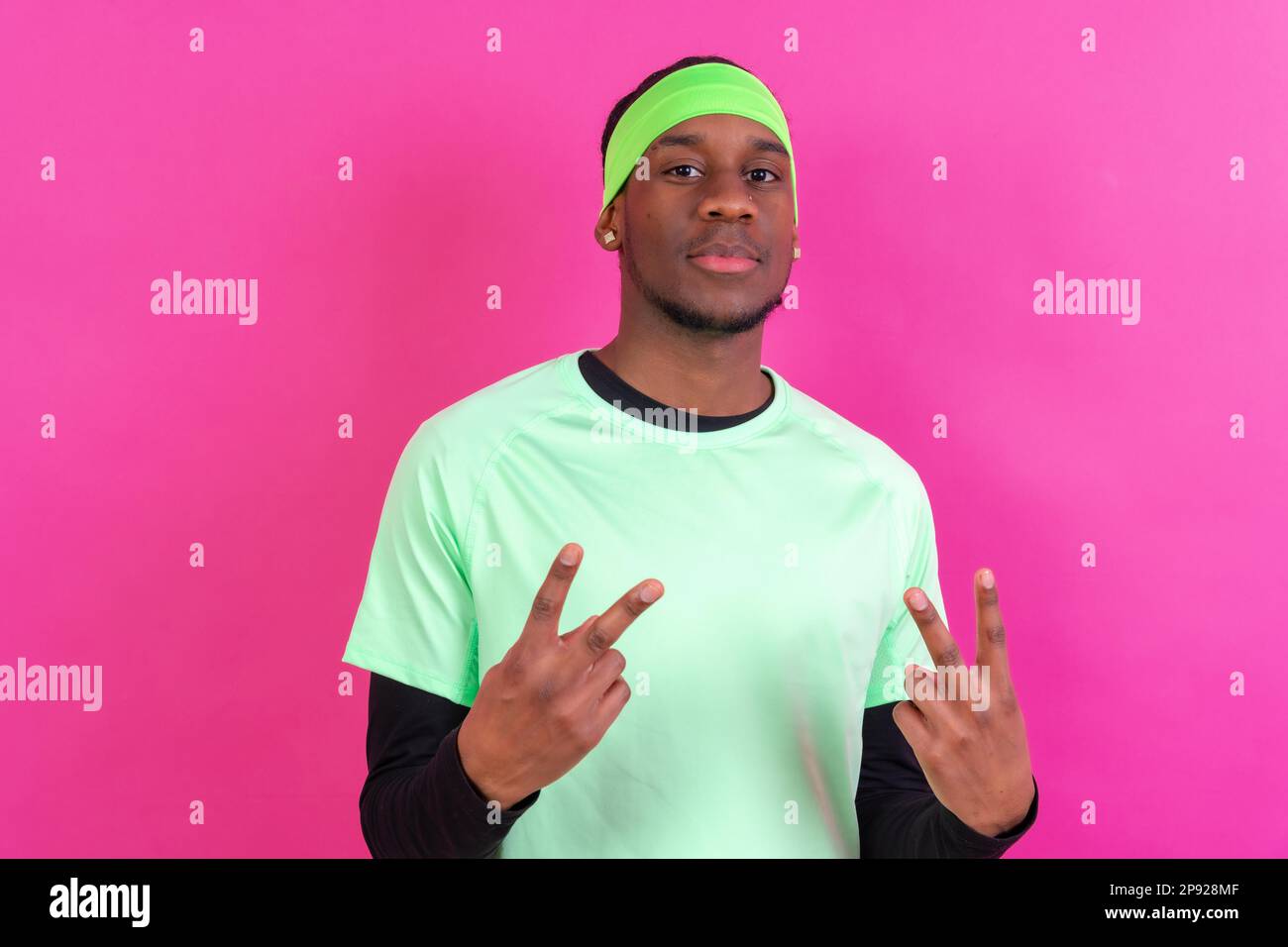 Black ethnic man in green clothes on a pink background, making the win gesture Stock Photo