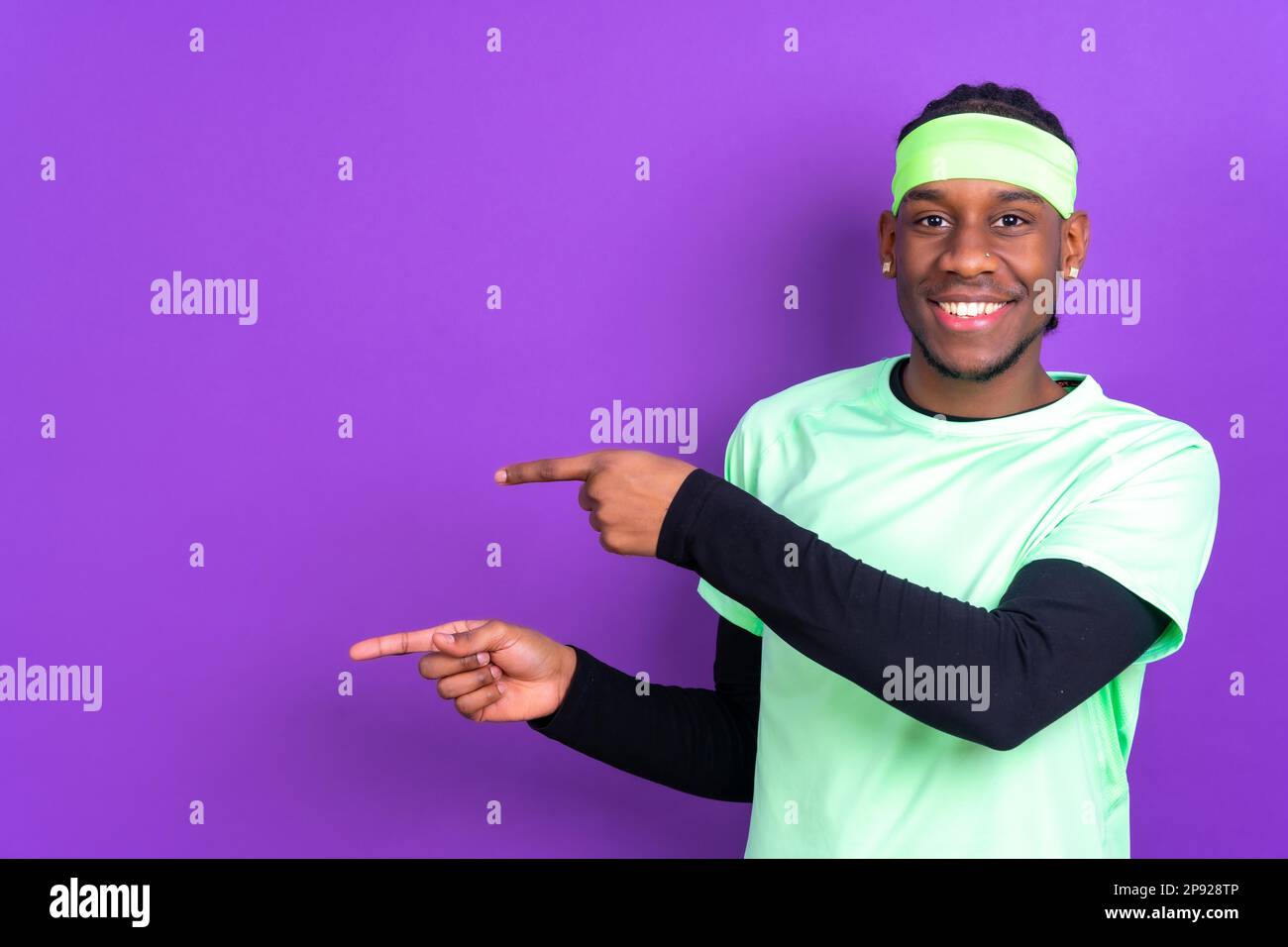 Black ethnic man in green clothes on a purple background, pointing at a free copy space Stock Photo
