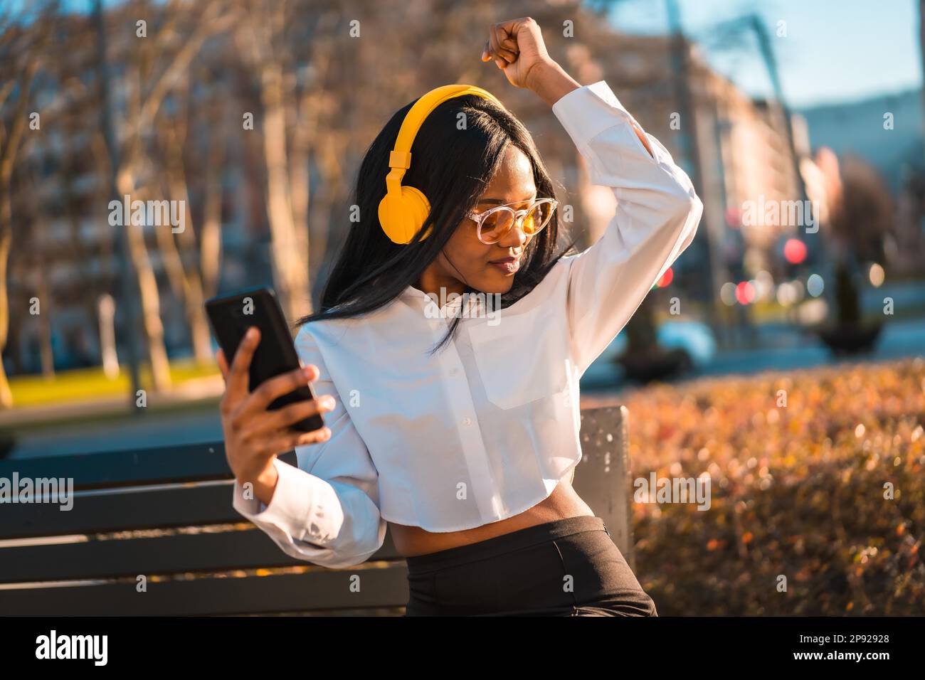 African american woman listening to music with headphones at sunset in the city, dancing Stock Photo